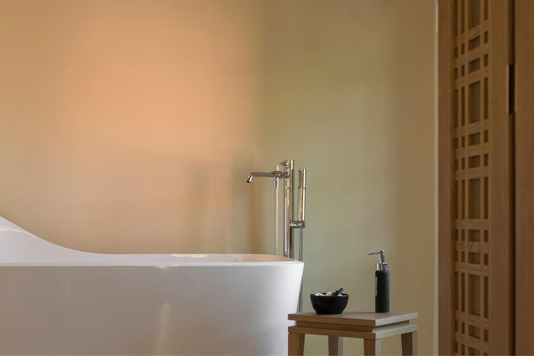 A soaking tub with warm ambient lighting beside a wooden shelf