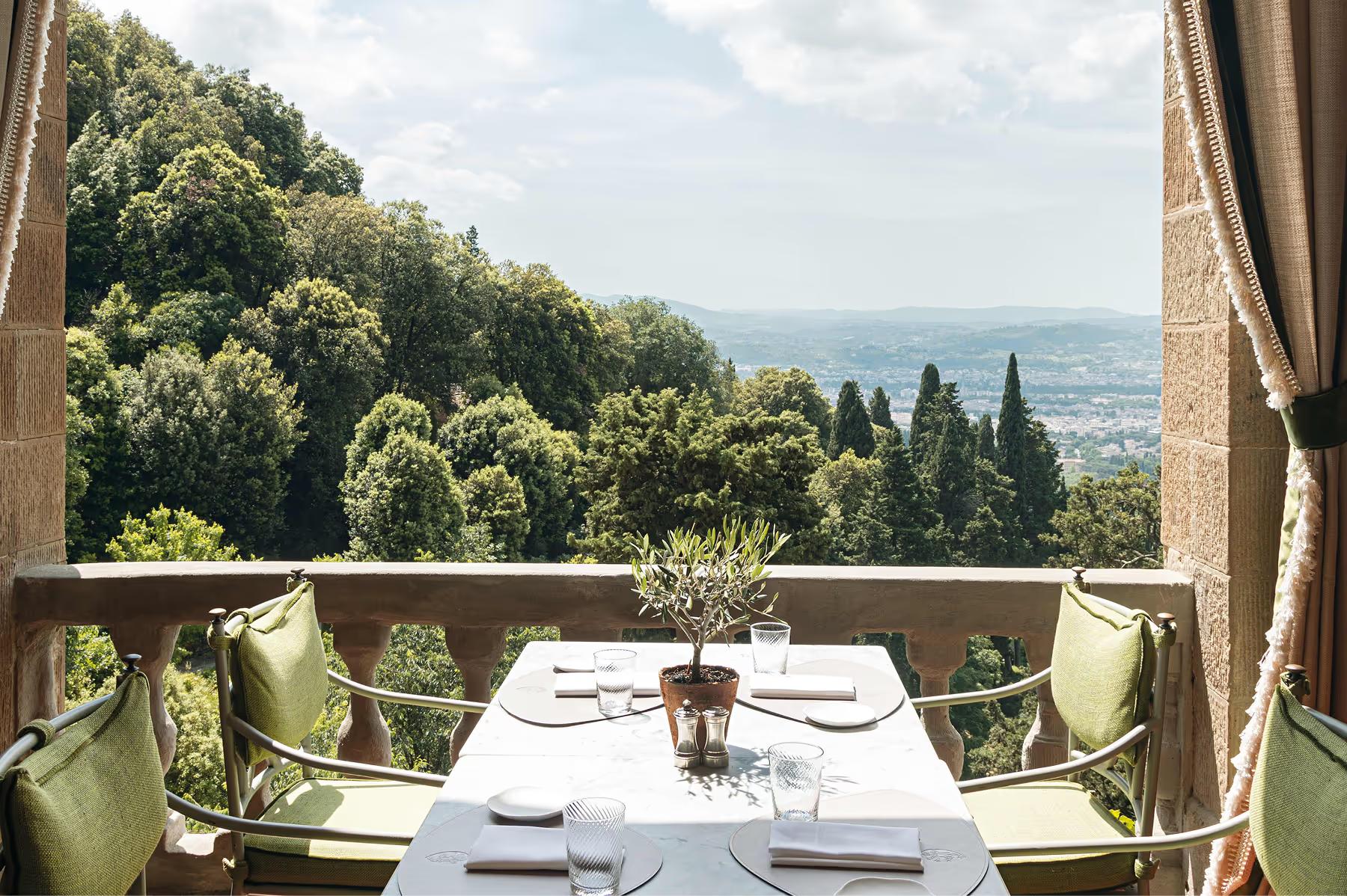 Villa San Michele: a table set for one on a terrace overlooking forested Tuscan hills and valleys below