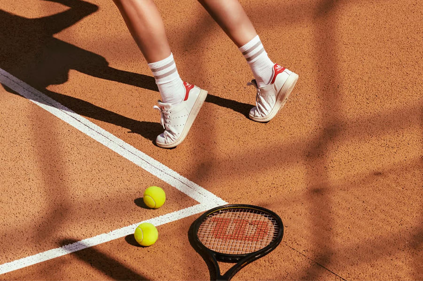Tennis court with athletic shoes, racket, and bright yellow balls on rust-colored clay