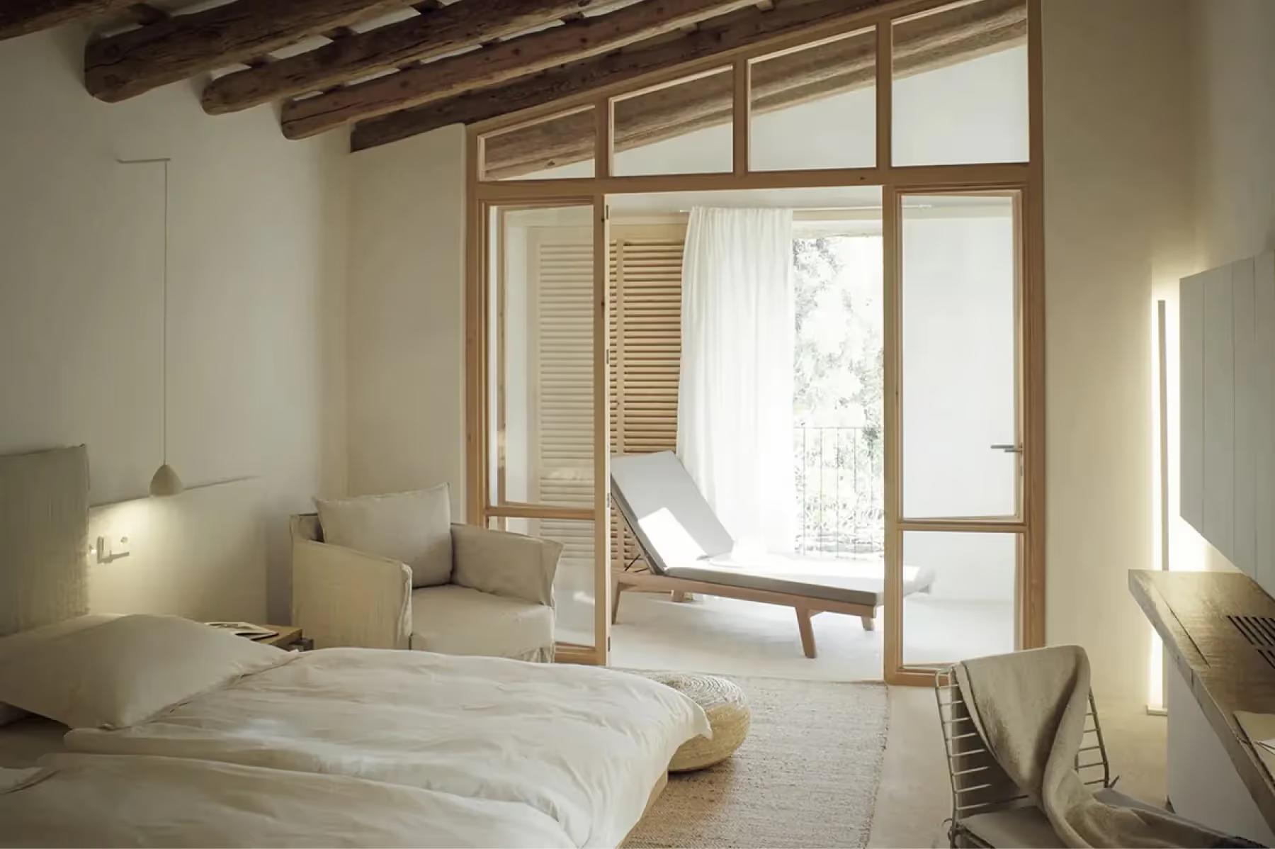 Serene minimalist bedroom with natural light from large windows, exposed wooden beams, and neutral linens