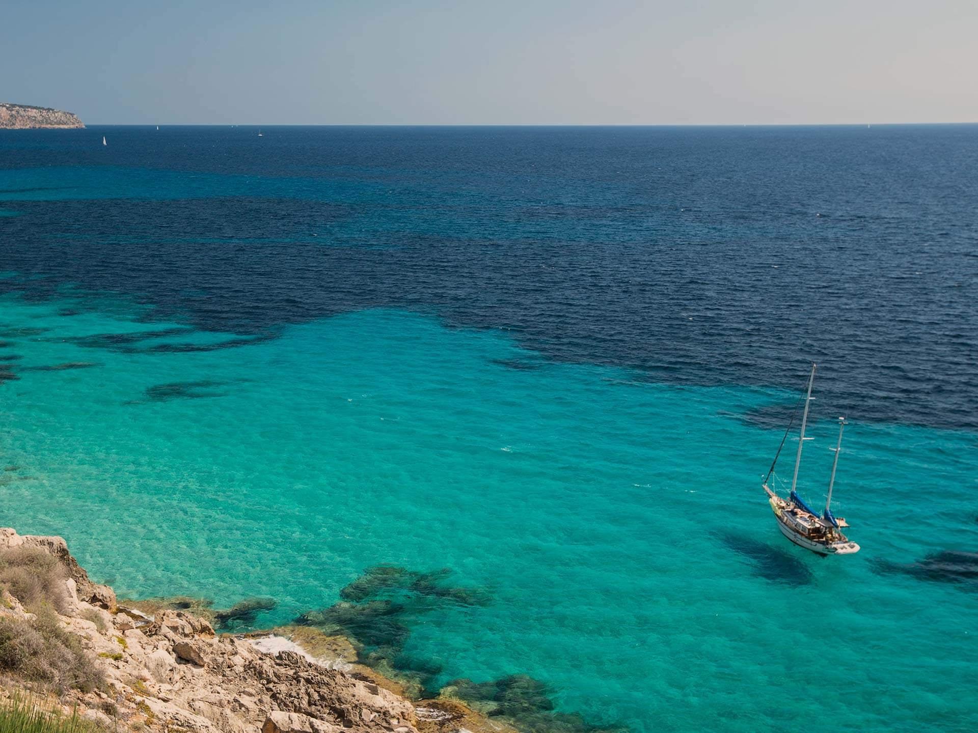 Cap Rocat: turquoise coves and pale limestone cliffs frame a moored sailboat in clear waters