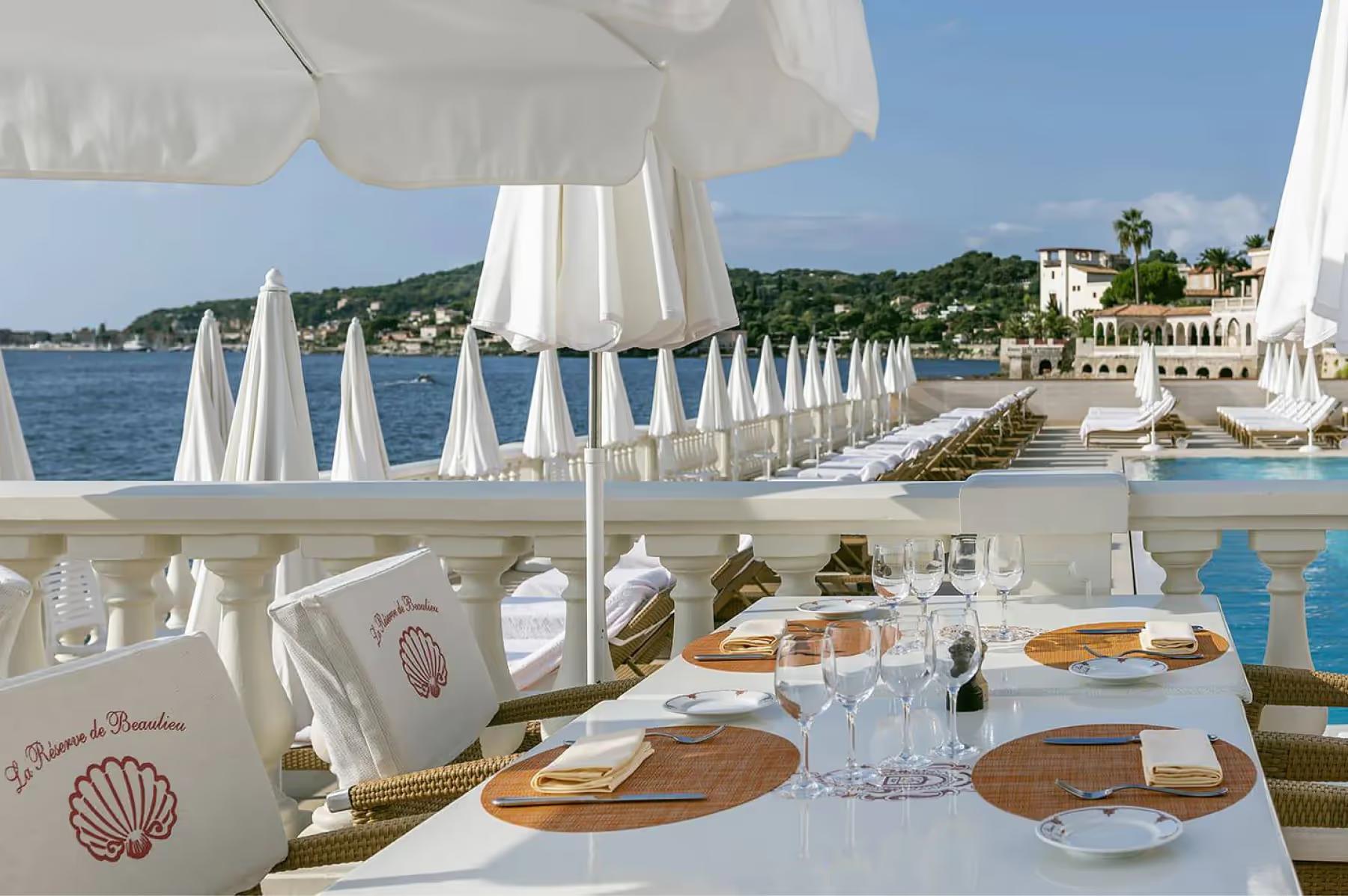 Beachside dining setup with table settings and Mediterranean vista