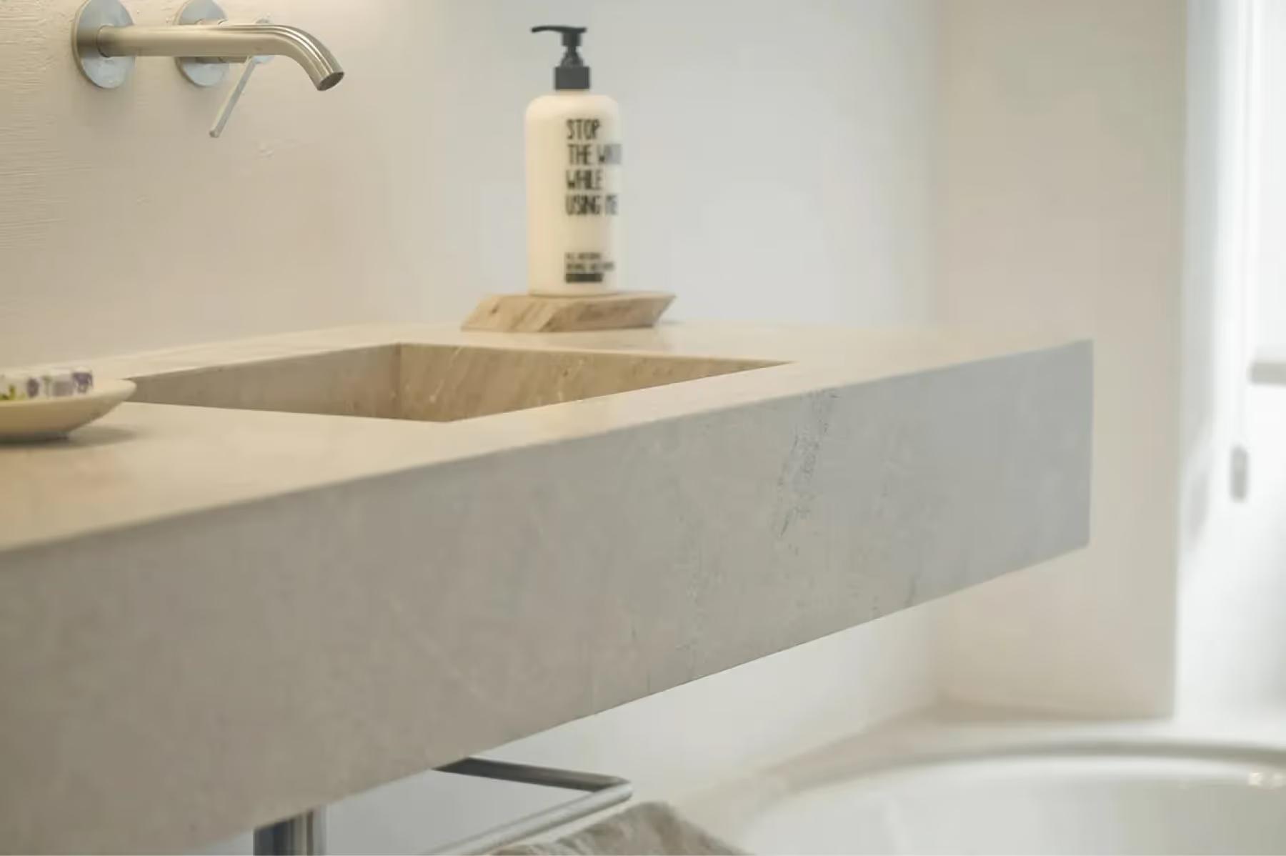 Es Racó d’Artà: minimalist concrete vanity with integrated sink, brass fixtures, and natural side lighting
