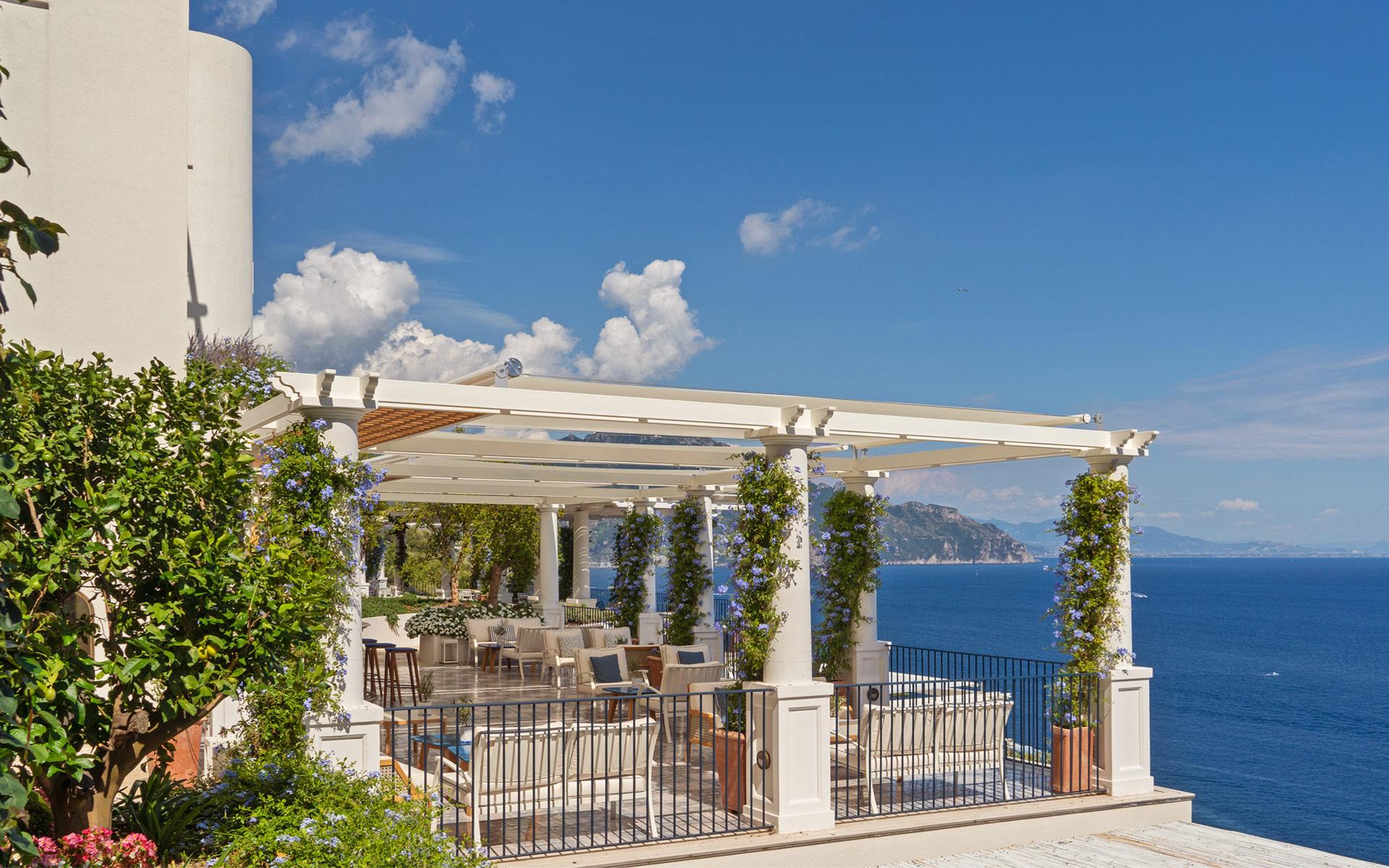 Borgo Santandrea: pergola dining area with white posts supporting climbing vines overlooking blue sea