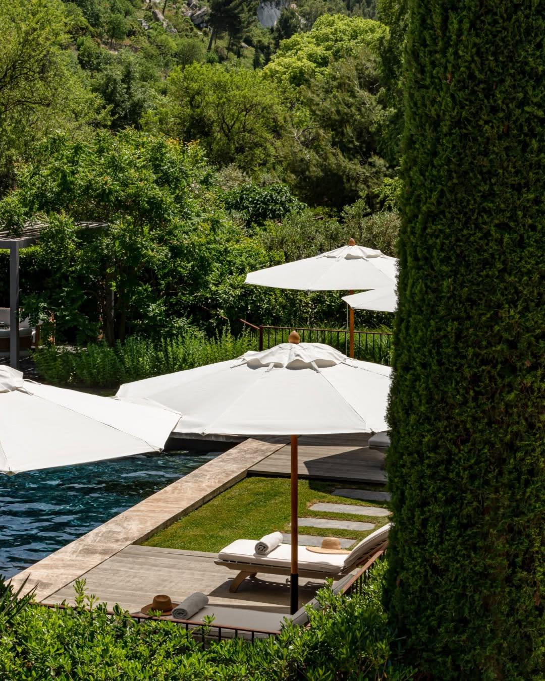 Hillside lounge terrace with tiered white shade sails, wooden loungers, cypress screens, valley horizon