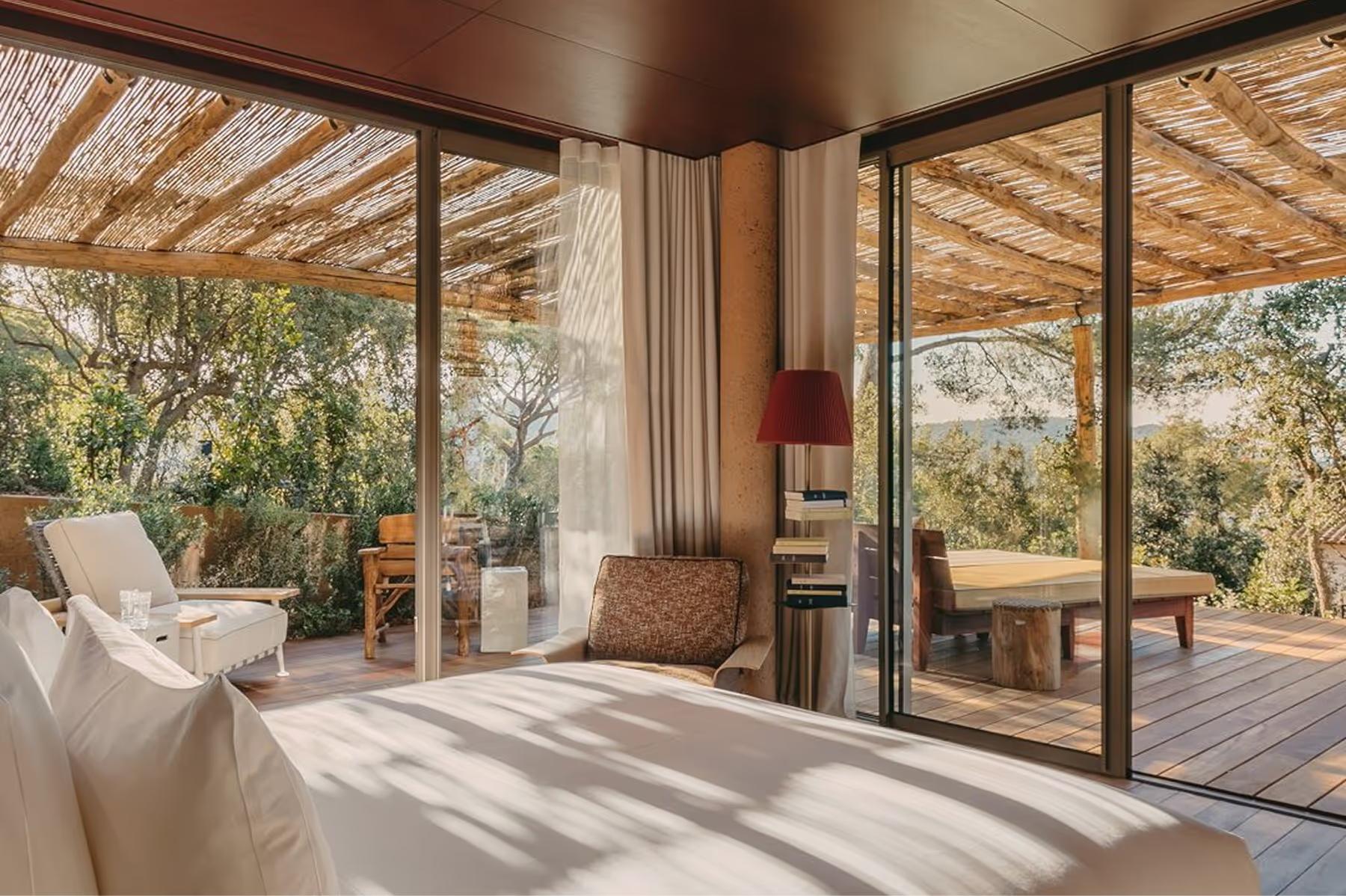 Bedroom with wooden ceiling and glass doors opening onto forested hillside view