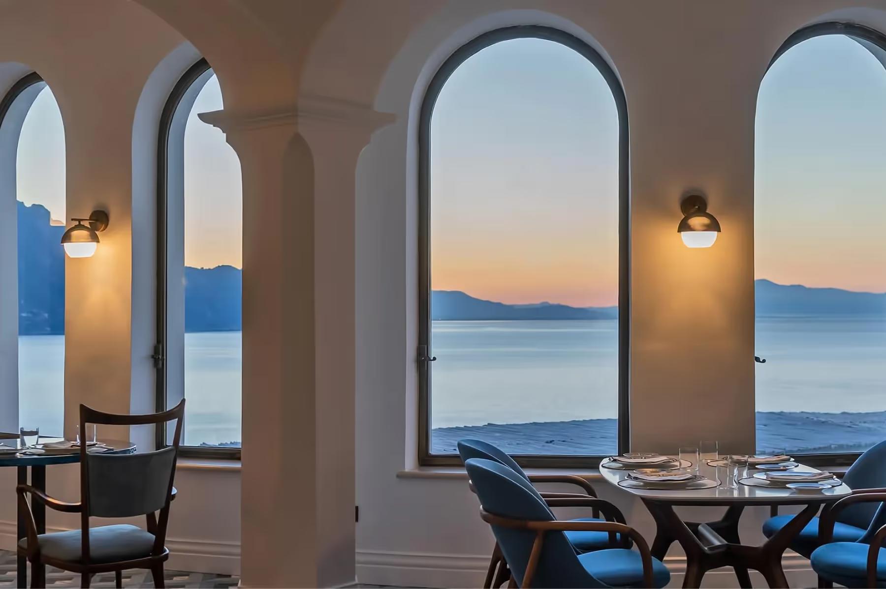 Indoor dining room with arched openings overlooking sunset seascape