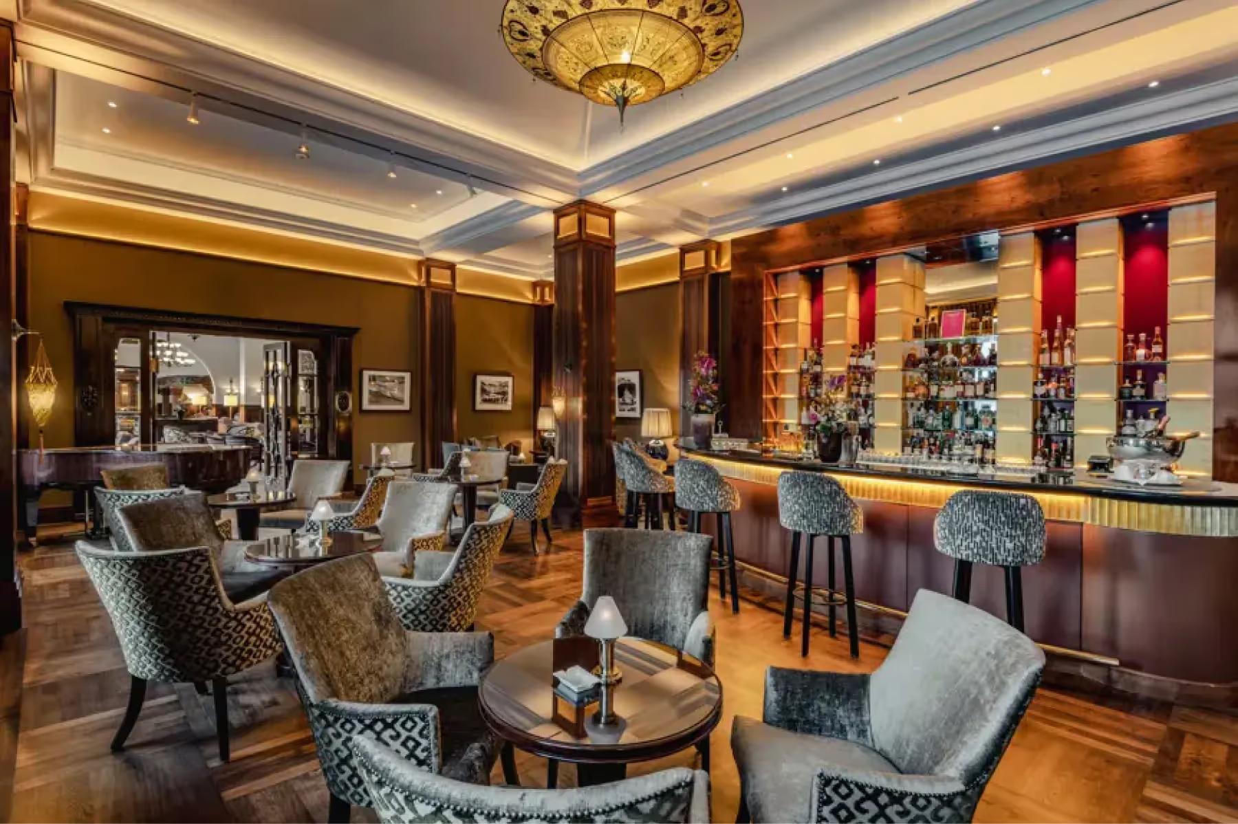 Suvretta House: a bar lounge with coffered ceiling, upholstered seating, and shelves of spirits and wines