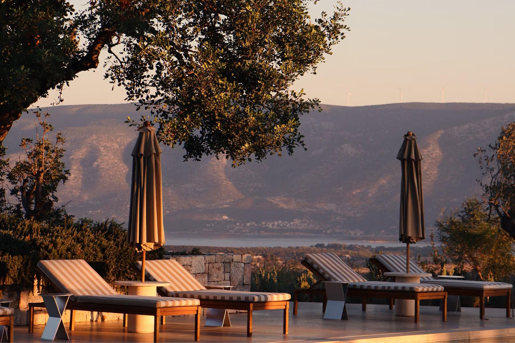 Amanzoe: stone terrace with poolside lounge and distant coastal views