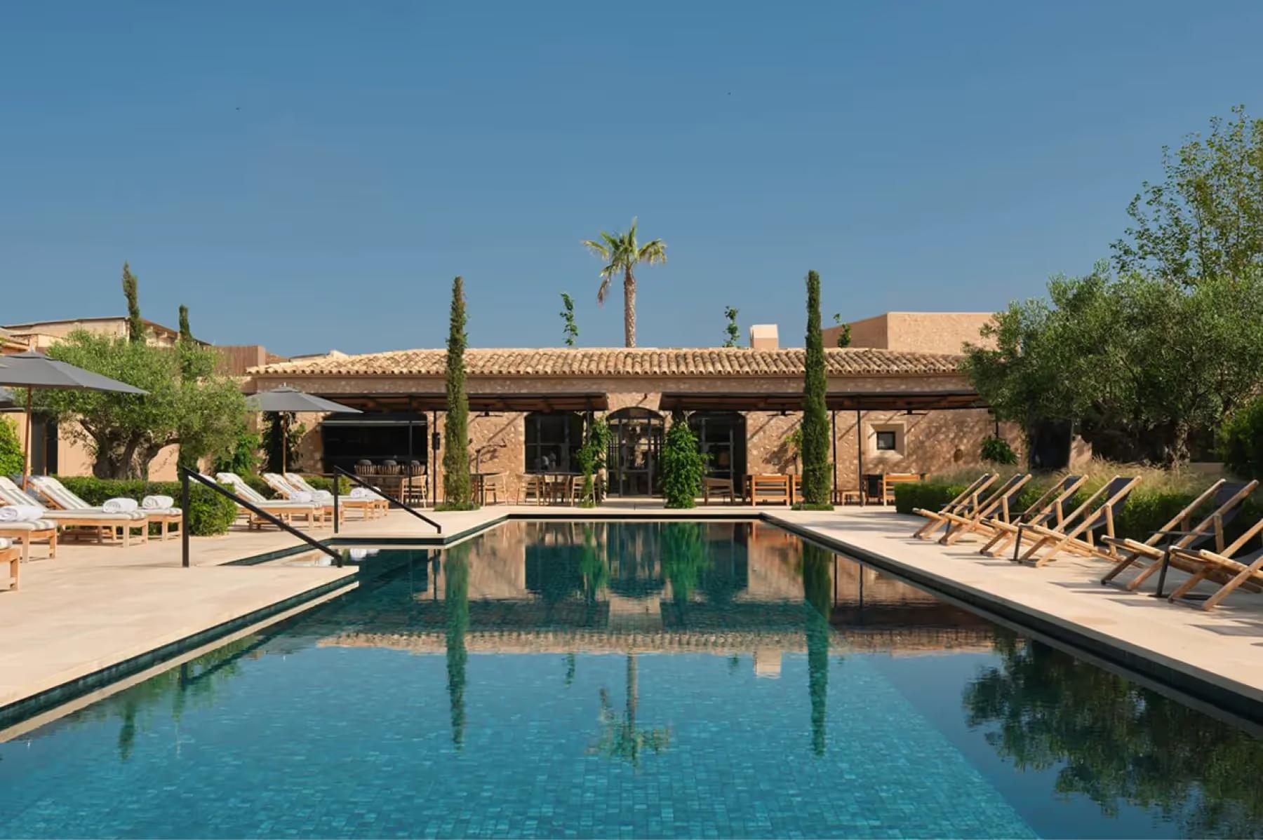 Can Ferrereta: outdoor pool surrounded by lounge chairs and terracotta mansion facade under blue sky