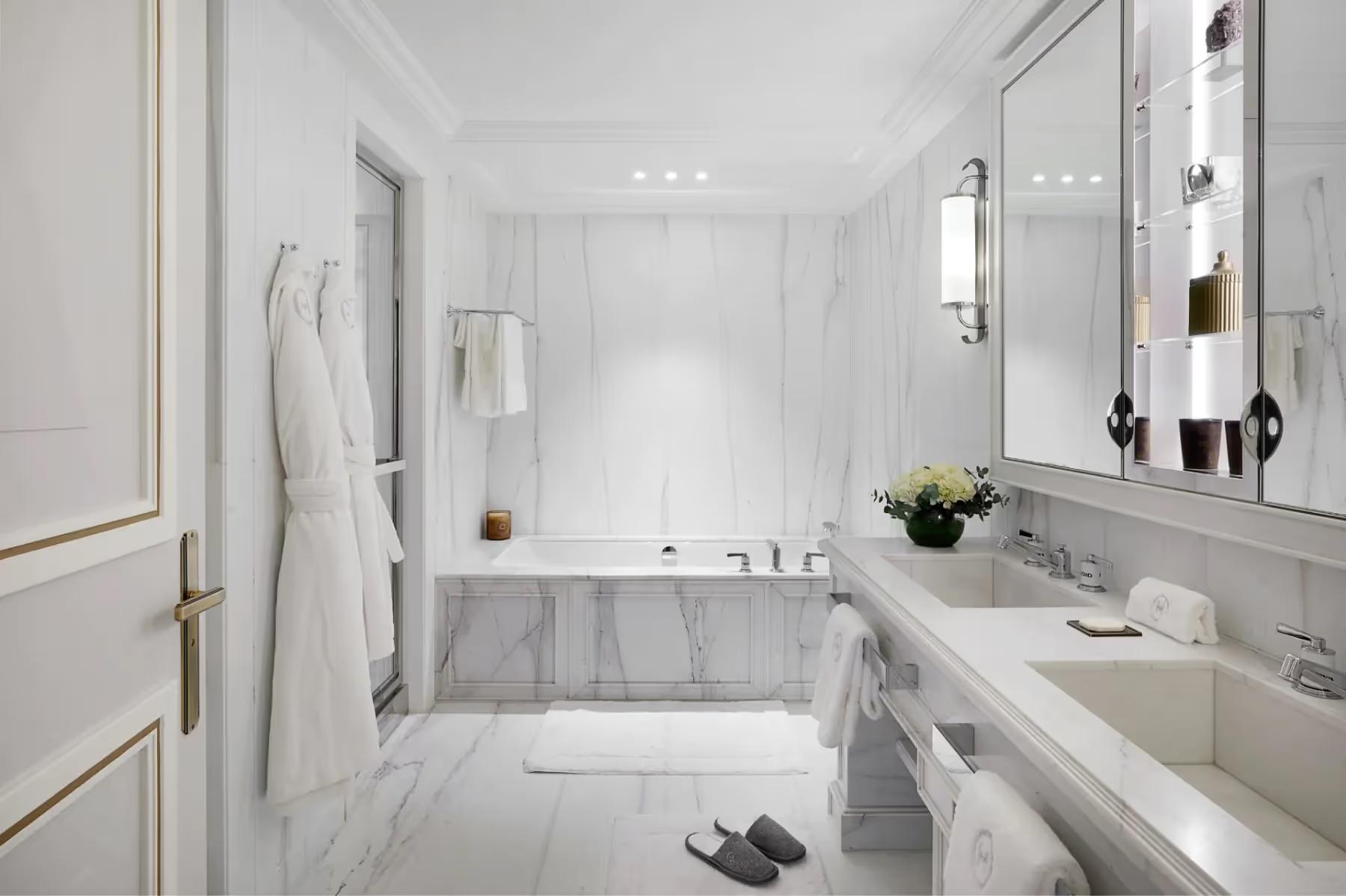 A bathroom with white marble walls, soaking tub, vessel sink, and marble floor