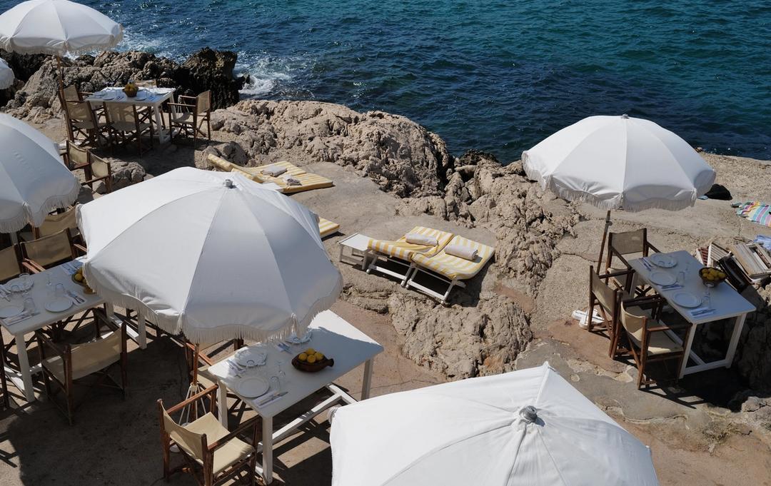The tables, parasols and loungers of Tuba Club spread across the rocks above the sea