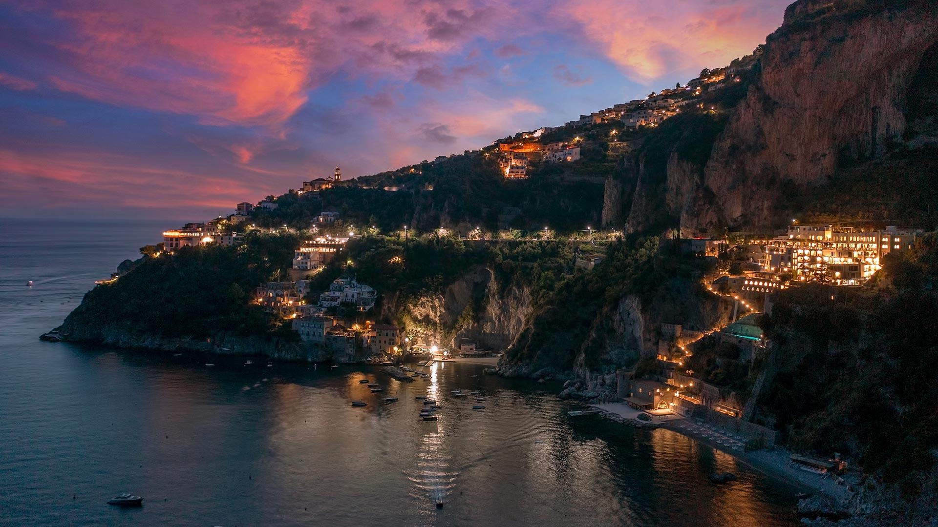 Borgo Santandrea: property exterior at night with warm lighting against dramatic rocky coastline backdrop