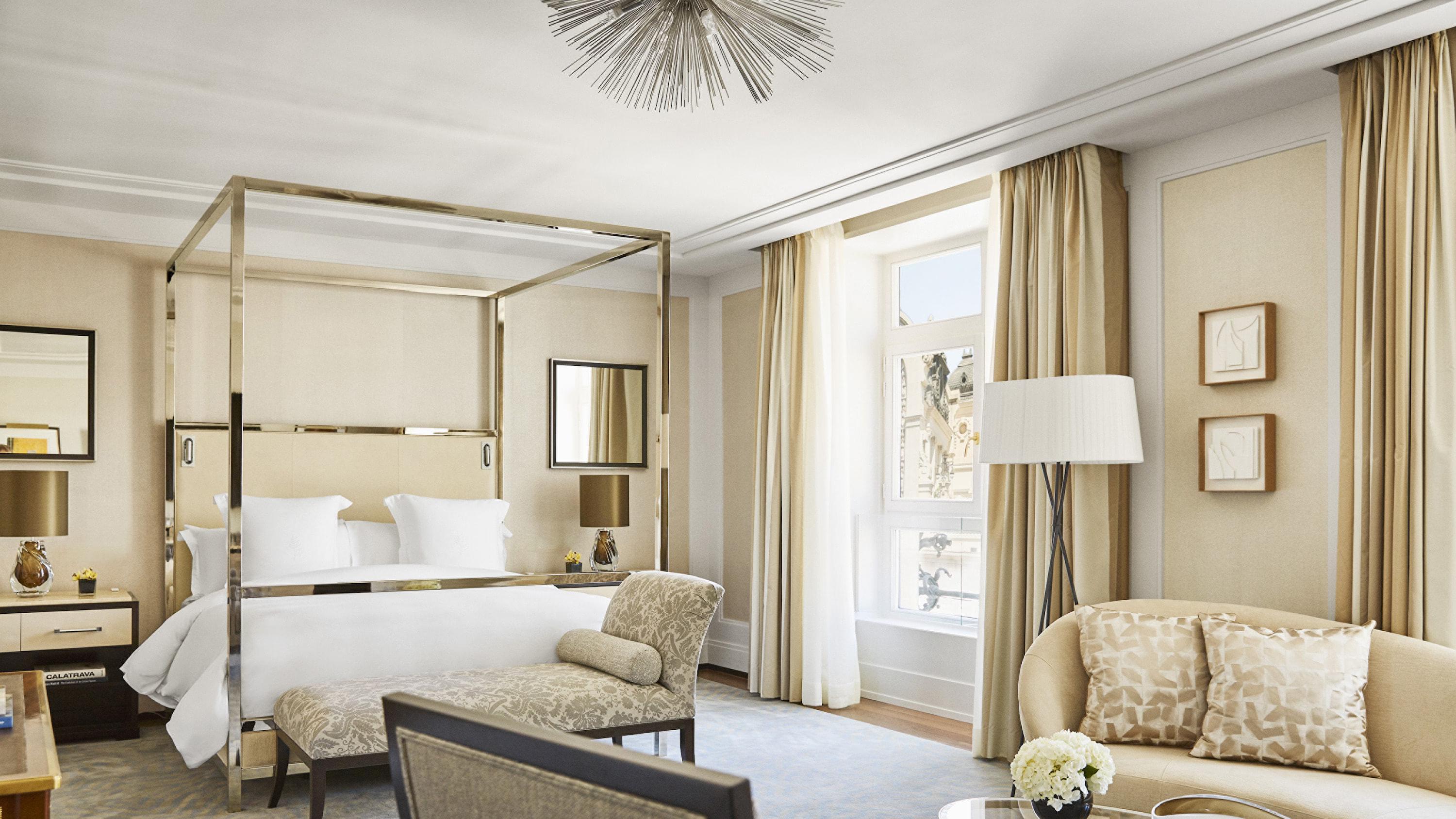 A canopy bed with gold framing and marble accents in a neutral suite with cream drapes and arched ceiling