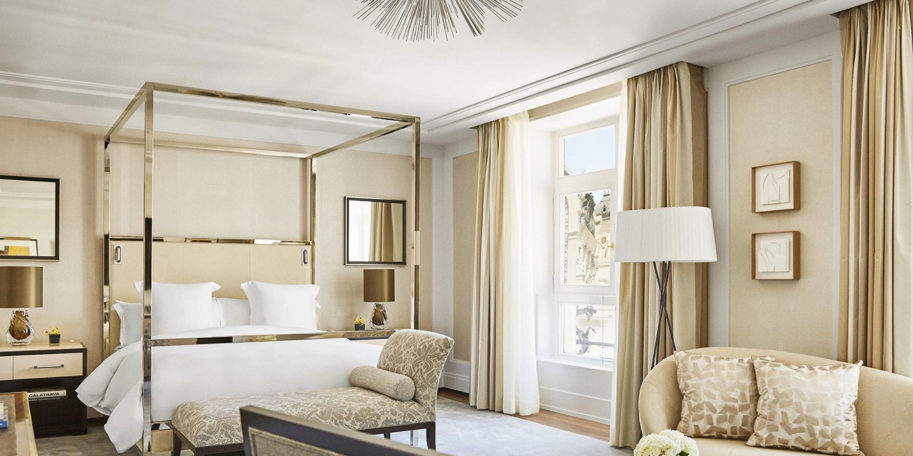 A canopy bed with gold framing and marble accents in a neutral suite with cream drapes and arched ceiling