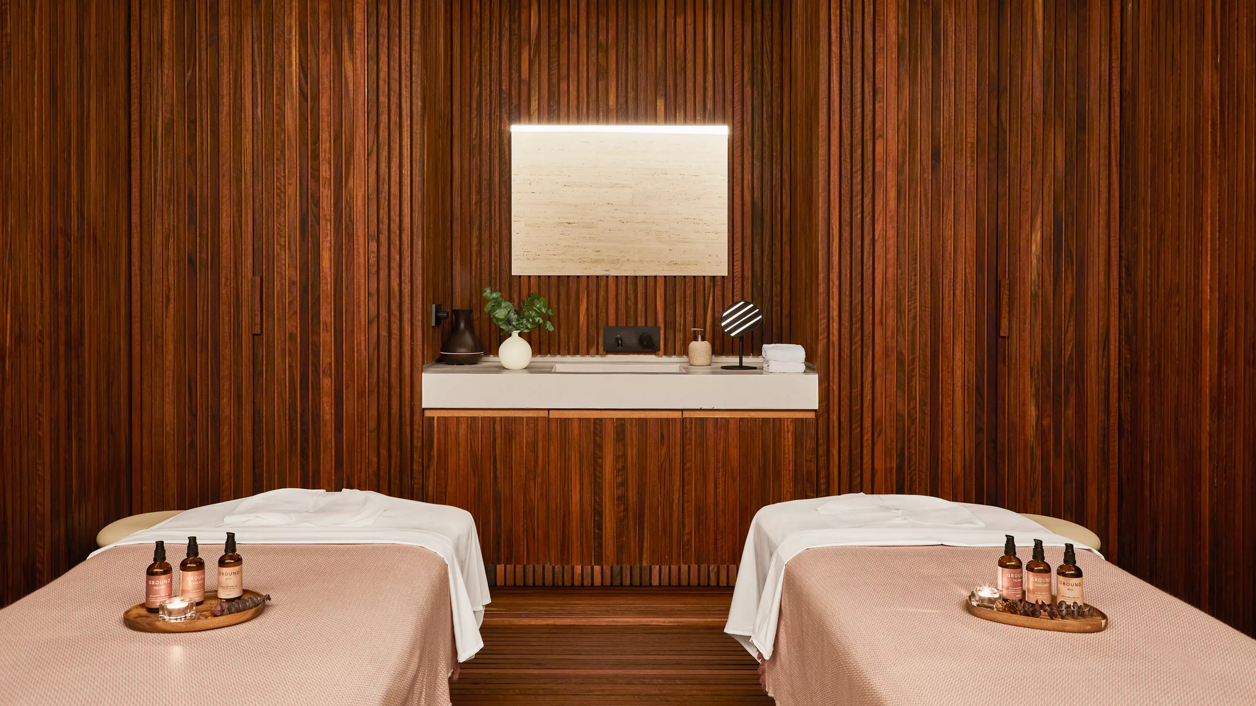 A treatment room with two massage tables, wood paneling, and warm ambient lighting