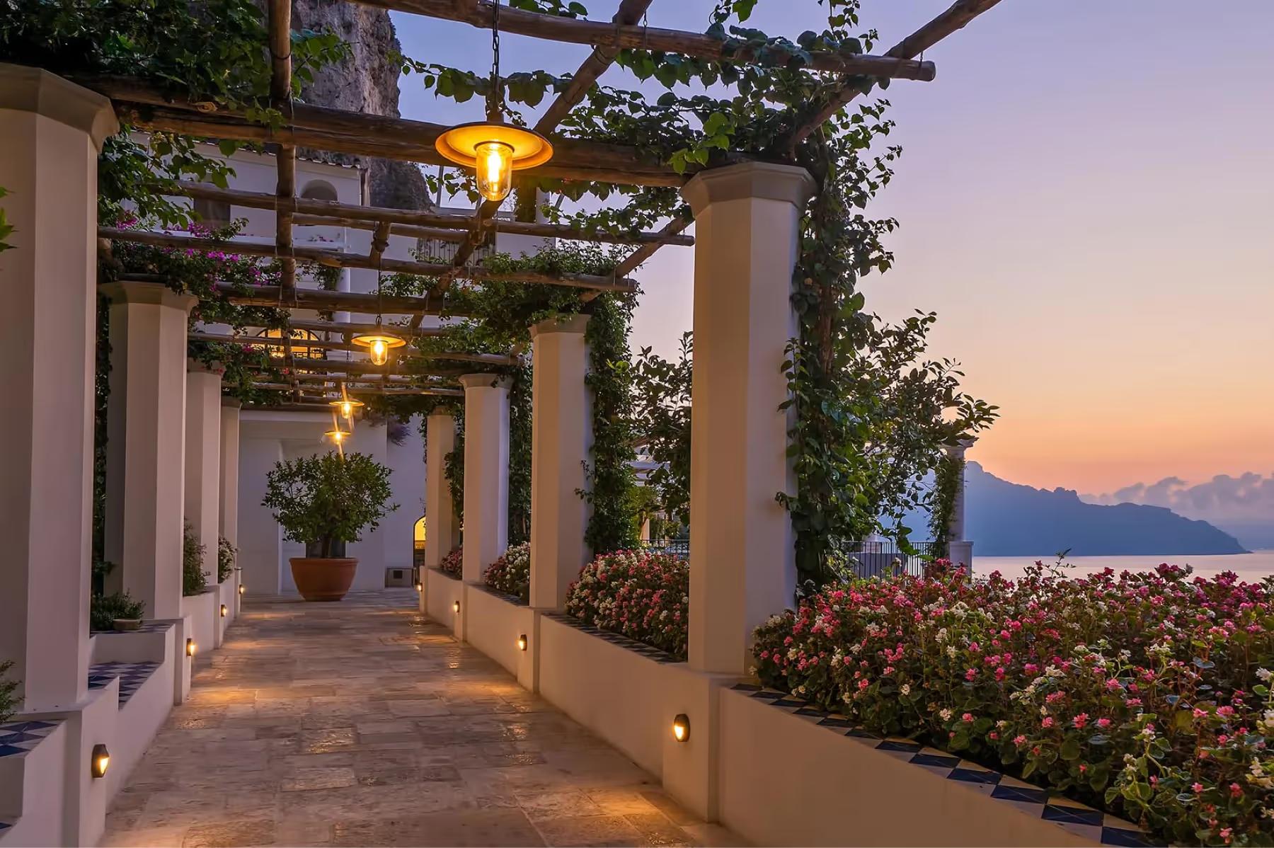 Borgo Santandrea: illuminated pergola pathway at dusk with climbing ivy and sea views in background