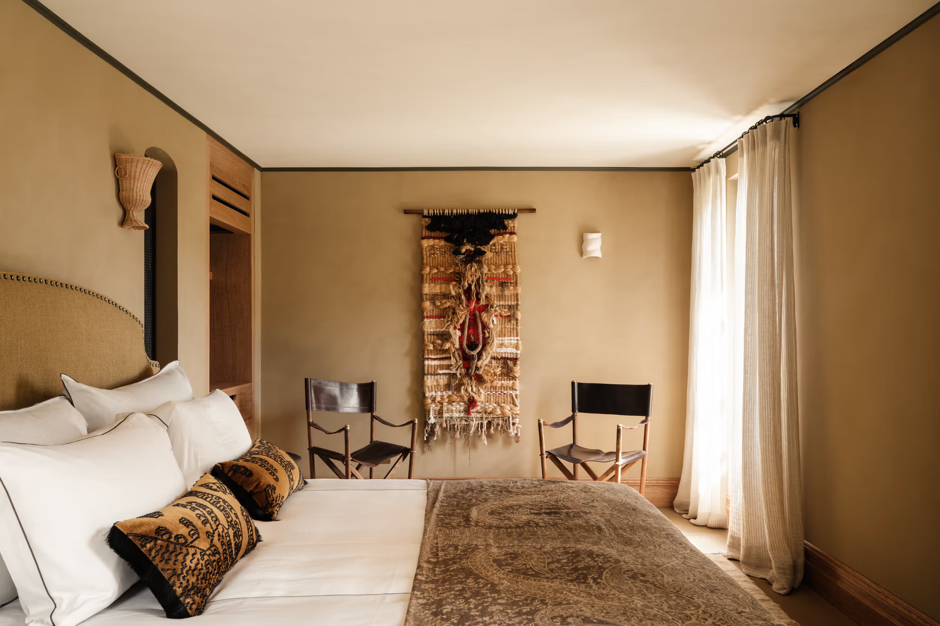 La Bergerie: ochre-toned bedroom with twin beds, patterned Berber pillows, woven textiles, rounded wooden doorway arch