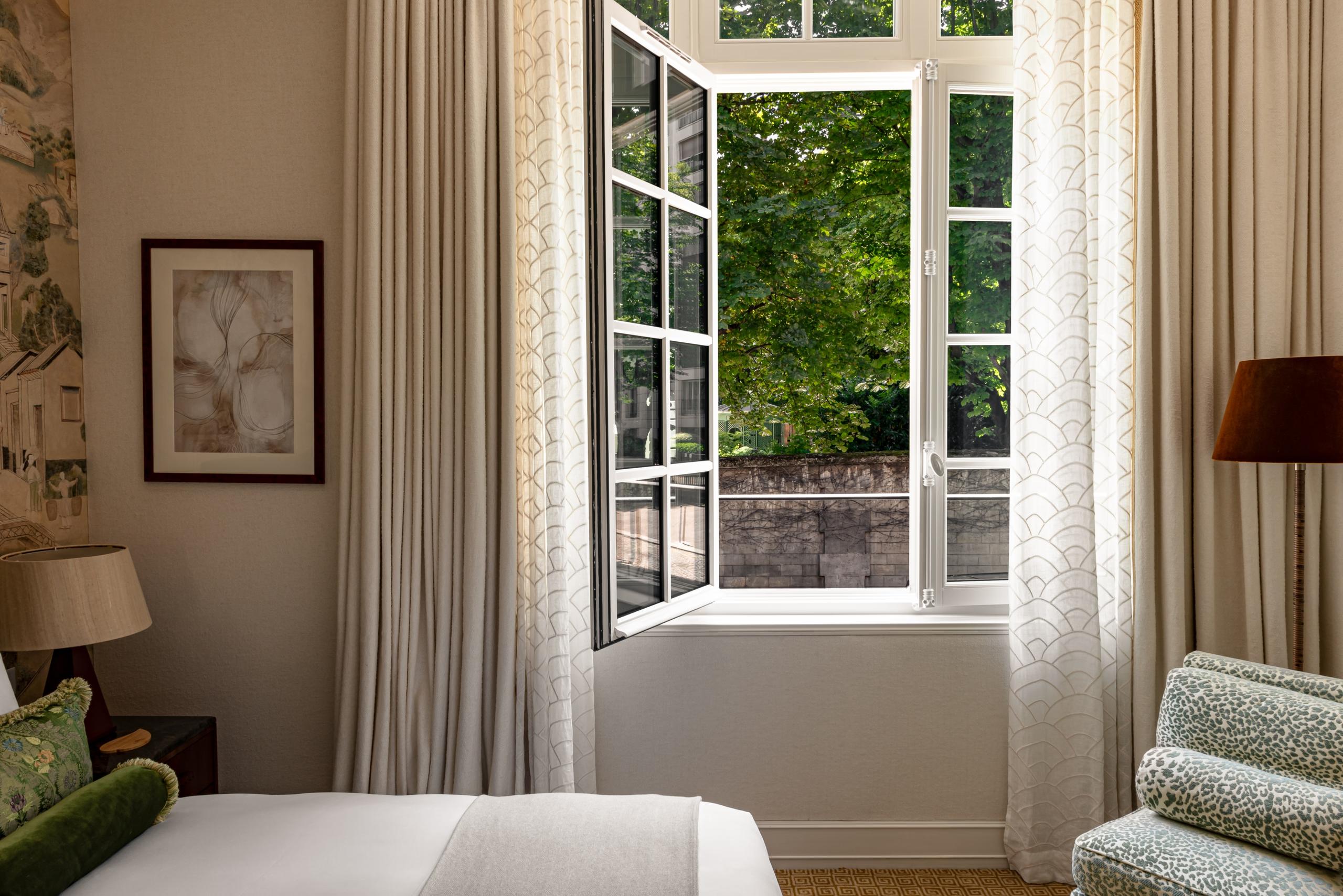 Saint James: guest bedroom with garden-view window, cream upholstered seating, and wood furnishings
