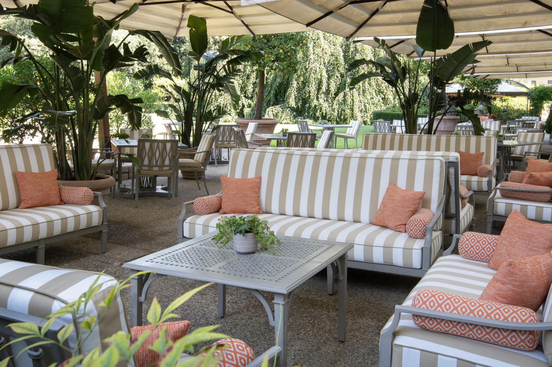 Four Seasons Hotel Firenze: garden dining pavilion with striped lounge seating, tropical plants, and orange cushions