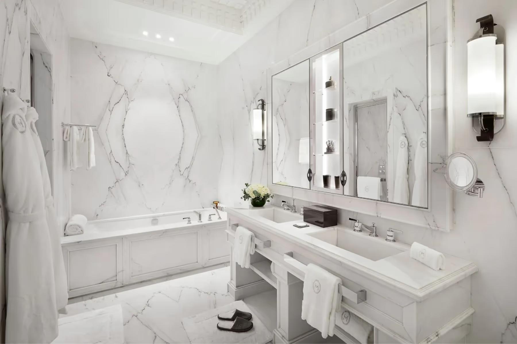 A marble bathroom with white tub, double vanity, and traditional sconce lighting