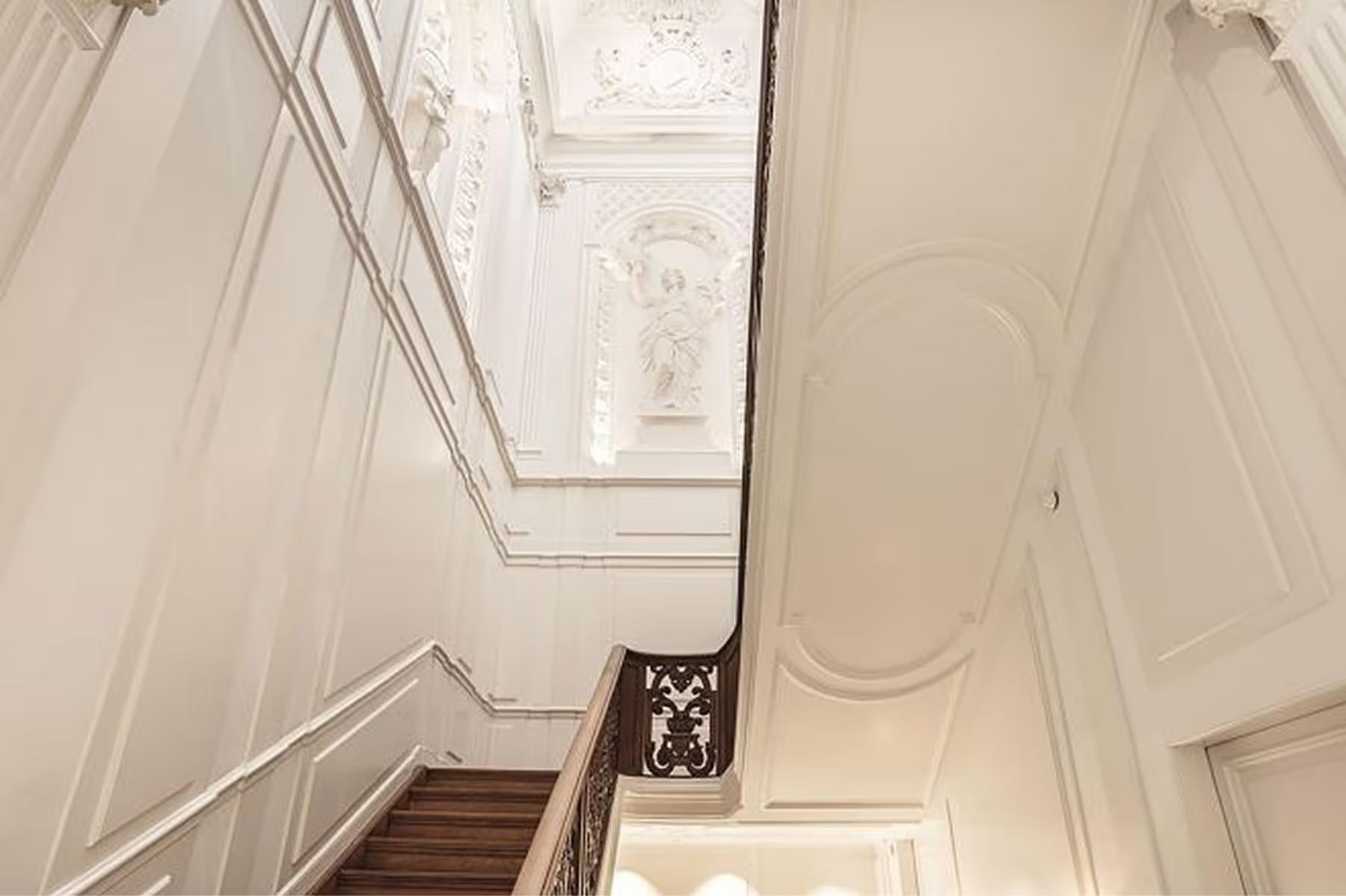 A stairwell with white paneled walls, arched skylight, and elegant railings creating a bright ascent