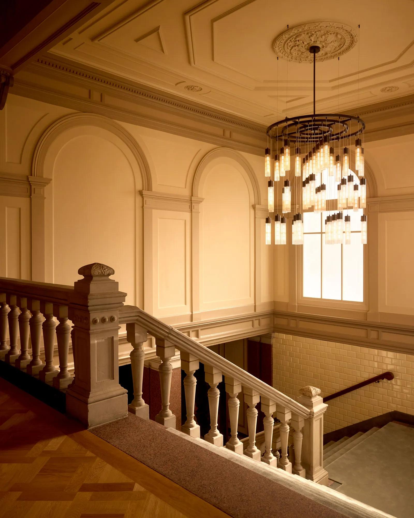 Rosewood Amsterdam: the historic staircase with a carved balustrade and a glass chandelier
