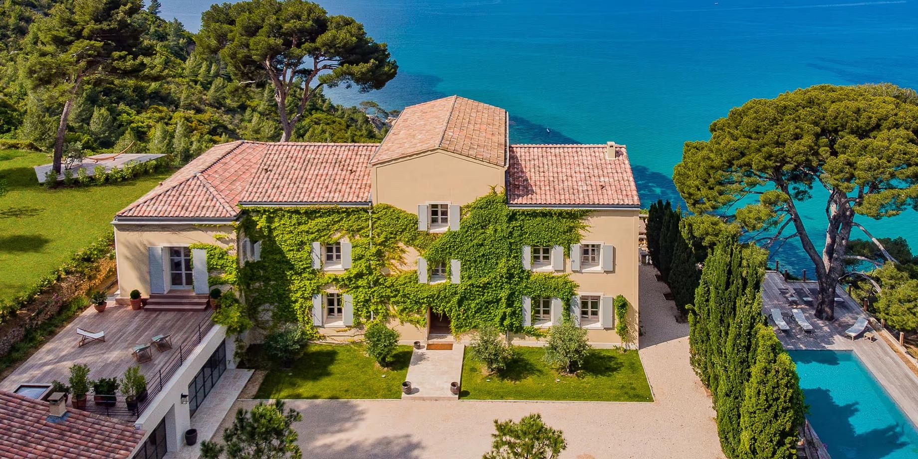 Terracotta villa with clay-tiled roof set on clifftop overlooking turquoise Mediterranean waters