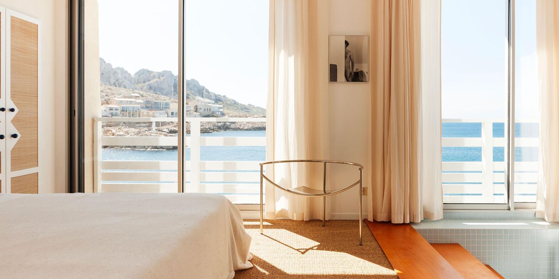 A cabanon bedroom at Tuba Club, its window open to the sea and the rocks of Les Goudes