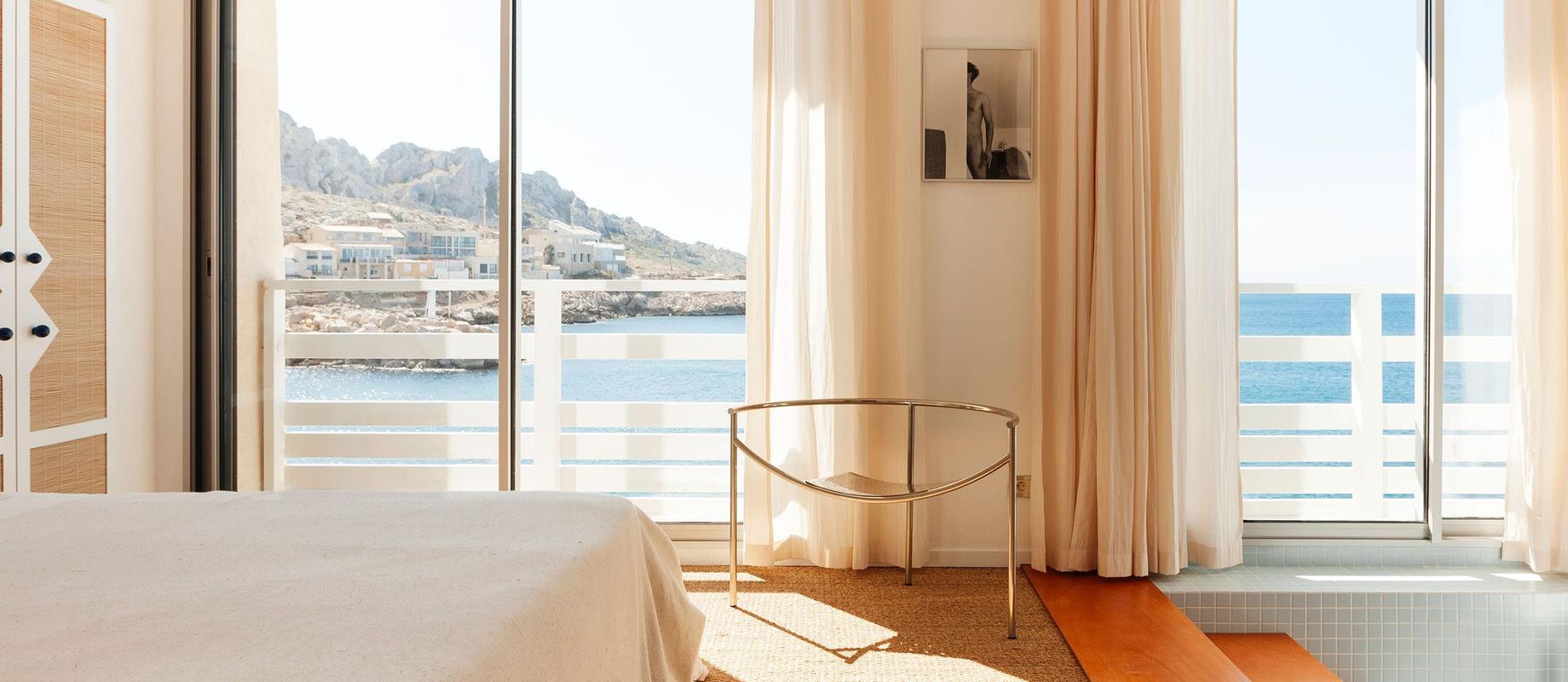 A cabanon bedroom at Tuba Club, its window open to the sea and the rocks of Les Goudes