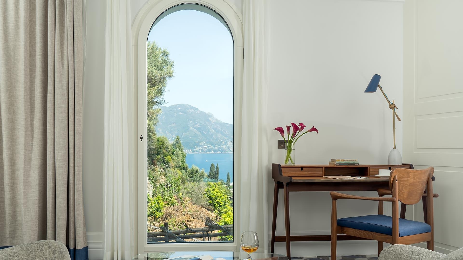 Borgo Santandrea: suite with arched opening framing mountain and sea views, midcentury furnishings