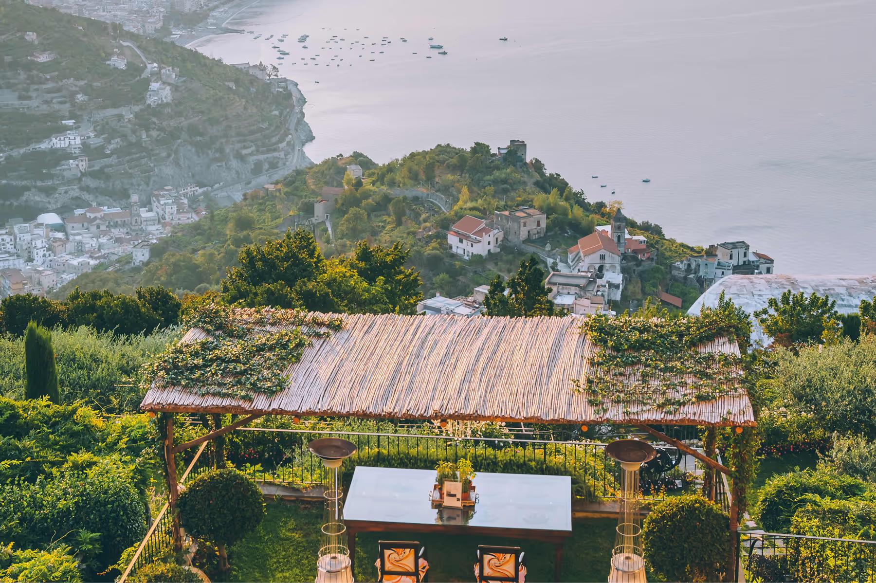 Caruso: aerial view of wooden pavilion with coastal dining setup on terraced gardens overlooking sea and village