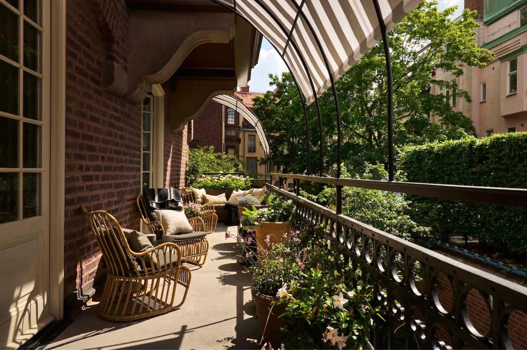 A wooden terrace deck with rattan chairs, iron railings, and mature trees overhead