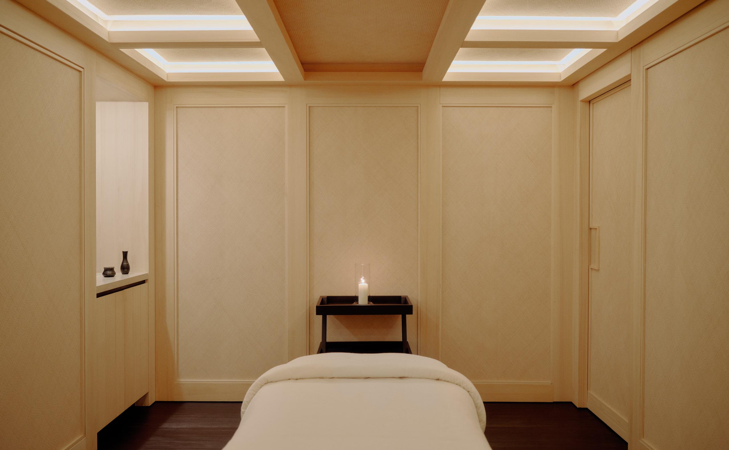 Spa treatment room with a backlit coffered ceiling and a single candle on a low table