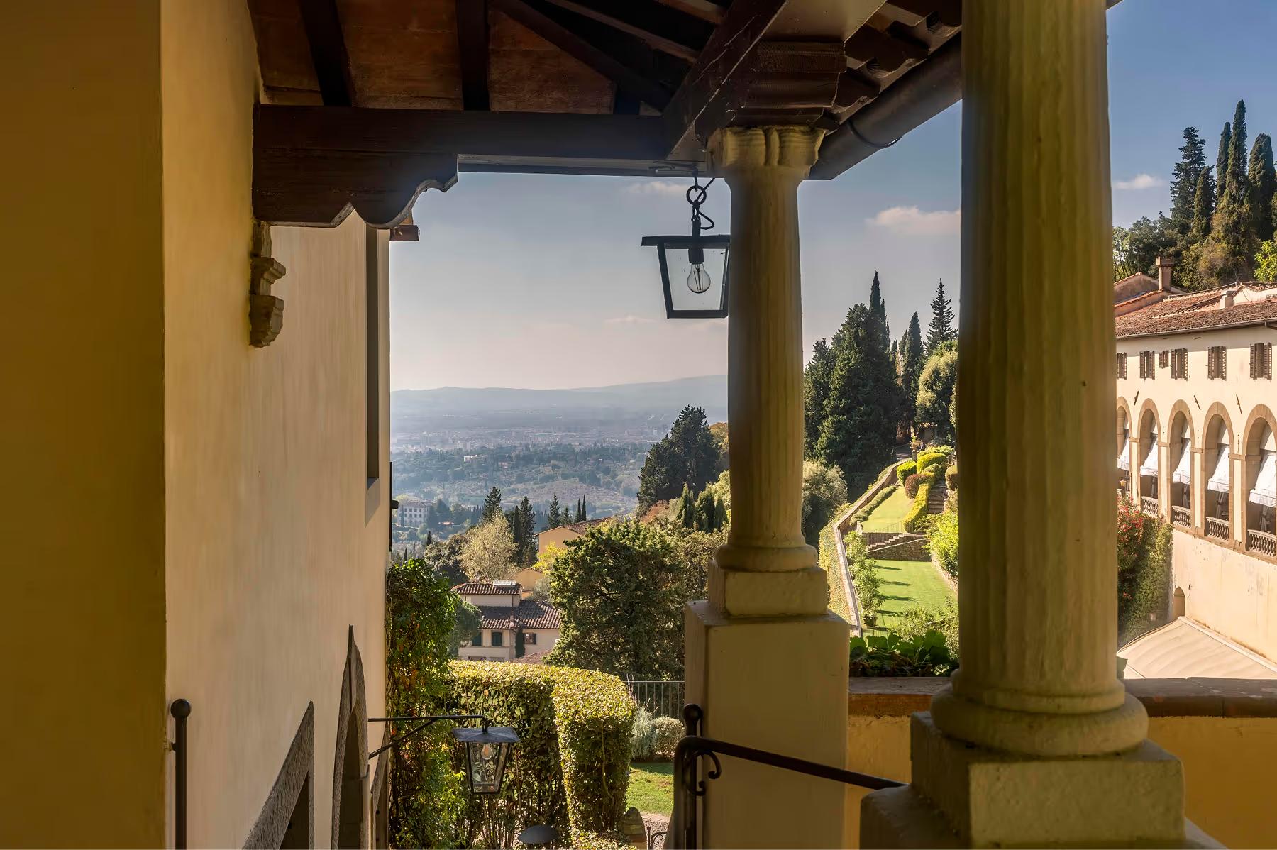Villa San Michele: cream loggia with stone columns, iron lantern, and expansive view across Florence valley with cypress trees