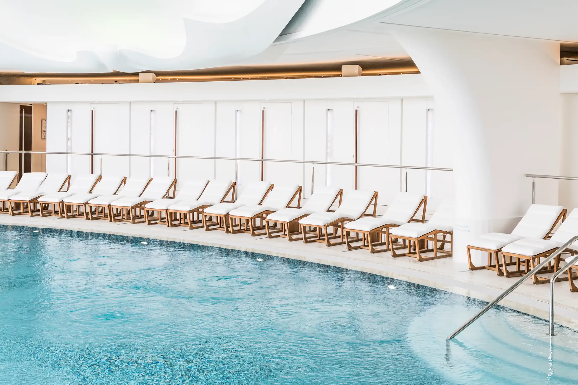 Hôtel de Paris Monte-Carlo: turquoise indoor pool with white cushioned loungers, bright skylights, and bronze ceiling beams