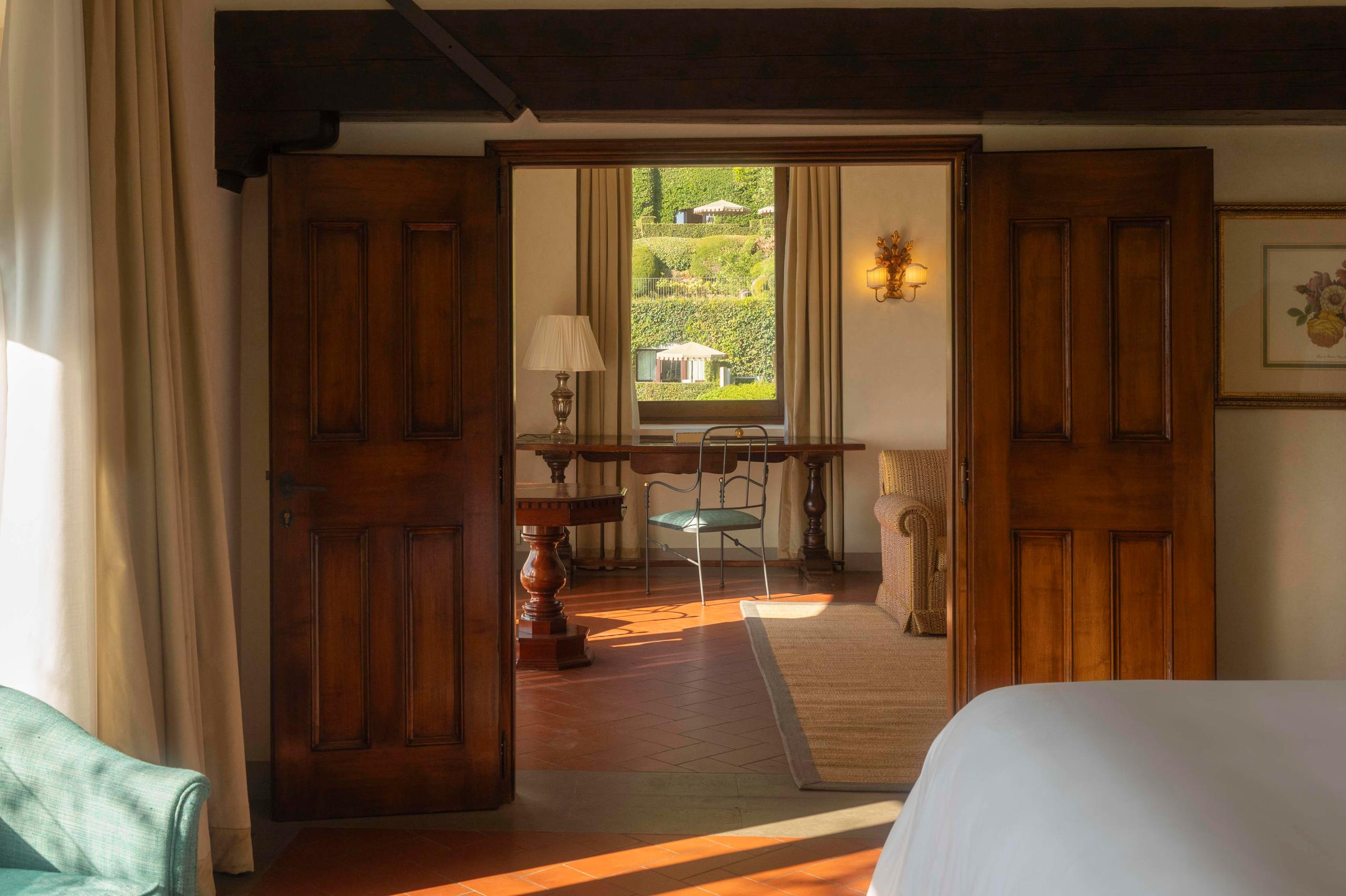 Villa San Michele: dark wooden doors opening to a room with warm sunlight, beamed ceilings, and terracotta flooring