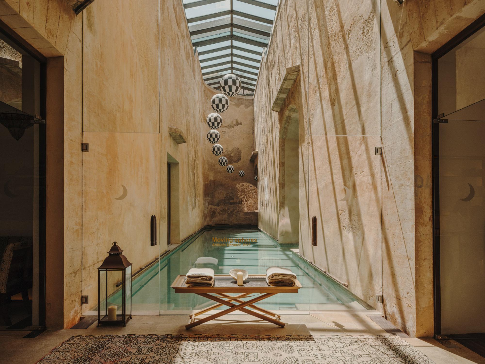 Cap Rocat: a spa corridor with turquoise pool, smooth stone walls, wooden columns, and glass skylight
