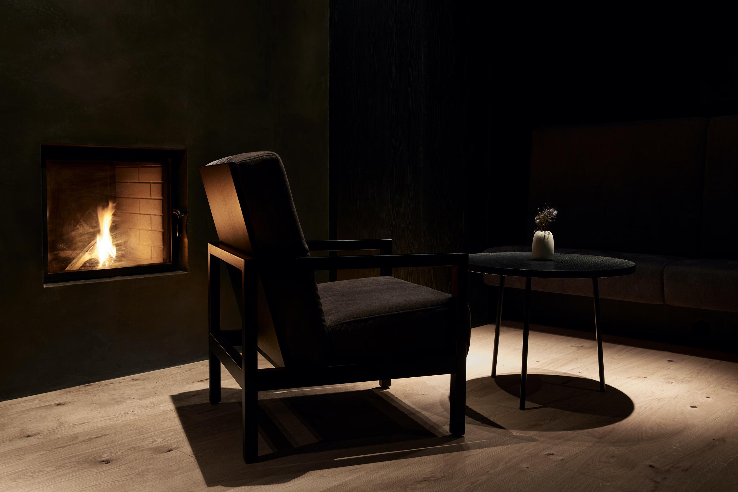 A cozy lounge corner with a modern fireplace insert, wood-frame chair, and soft ambient lighting
