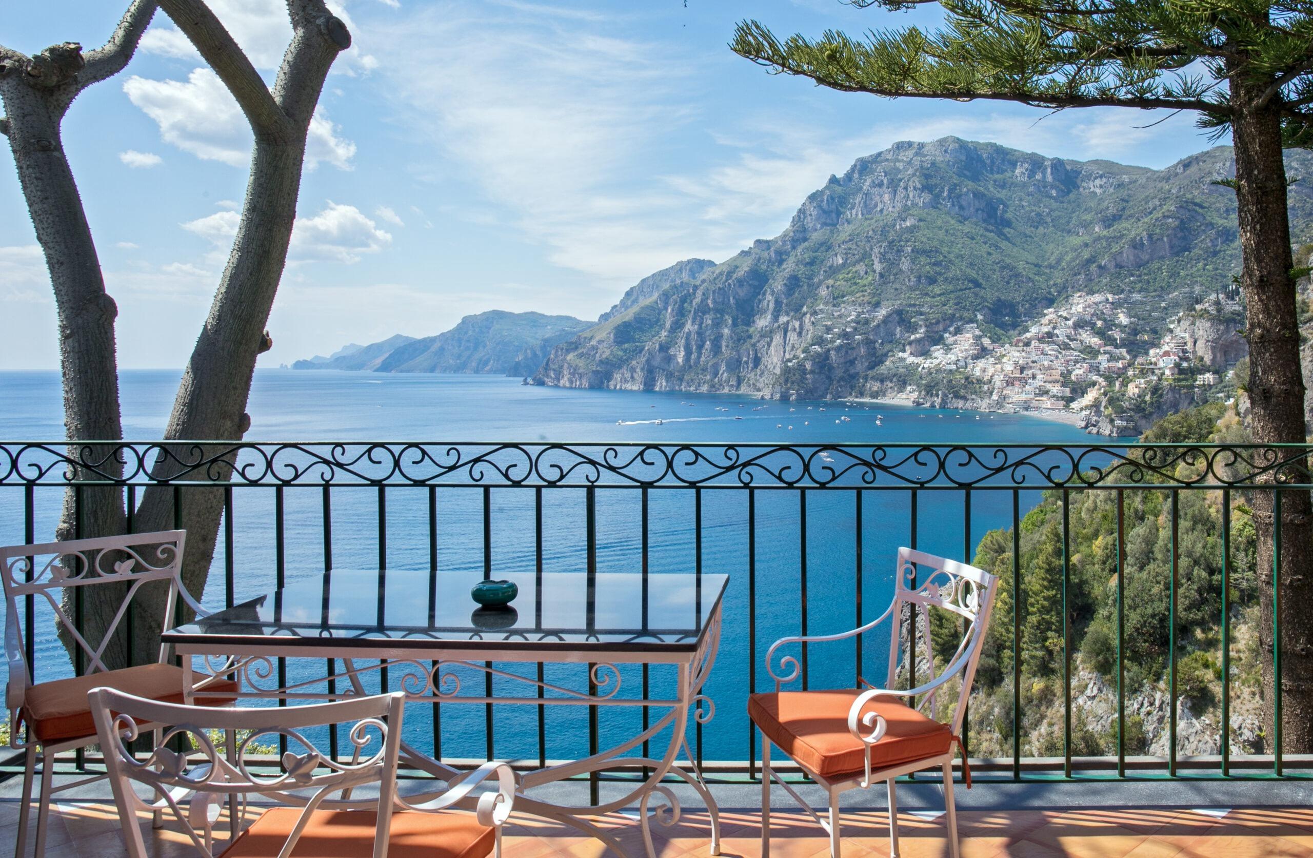Furnished terrace with sea views through iron railing, lounge chairs with orange cushions, Mediterranean vista