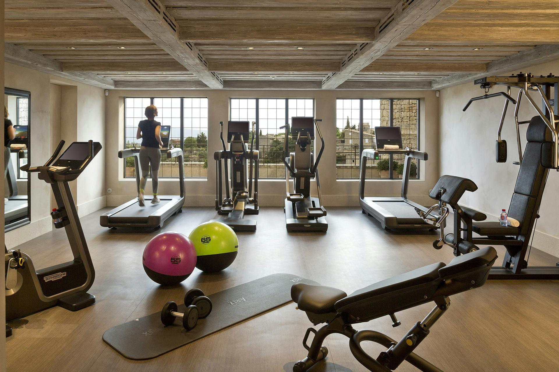 Airelles Gordes, La Bastide: fitness room with exercise equipment and valley views through windows
