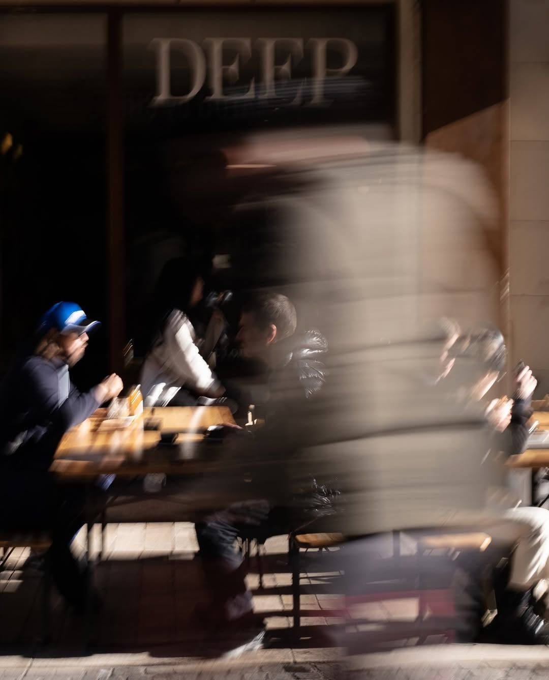 A passerby blurs past the outdoor tables under the Deep Coffee Roasters sign