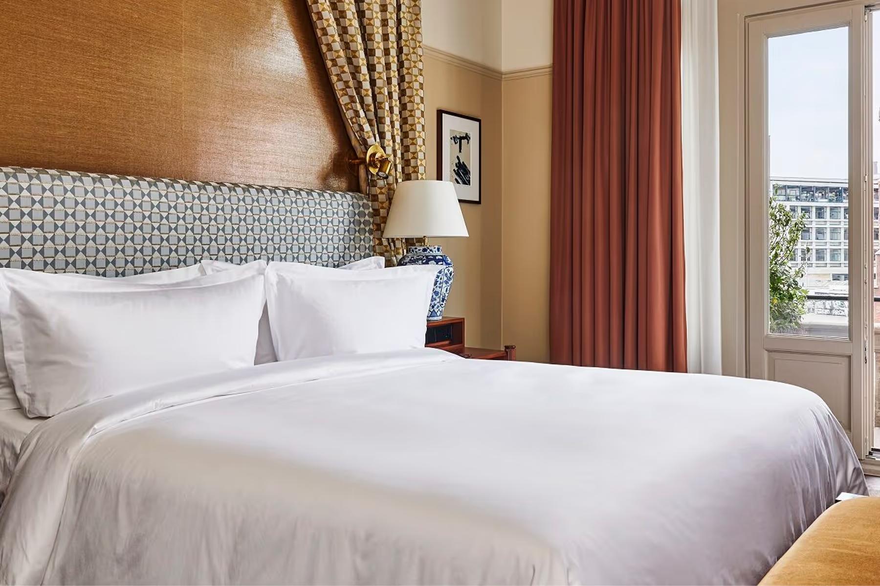 De L’Europe Amsterdam: bed with neutral linens, patterned headboard, and river view through tall windows