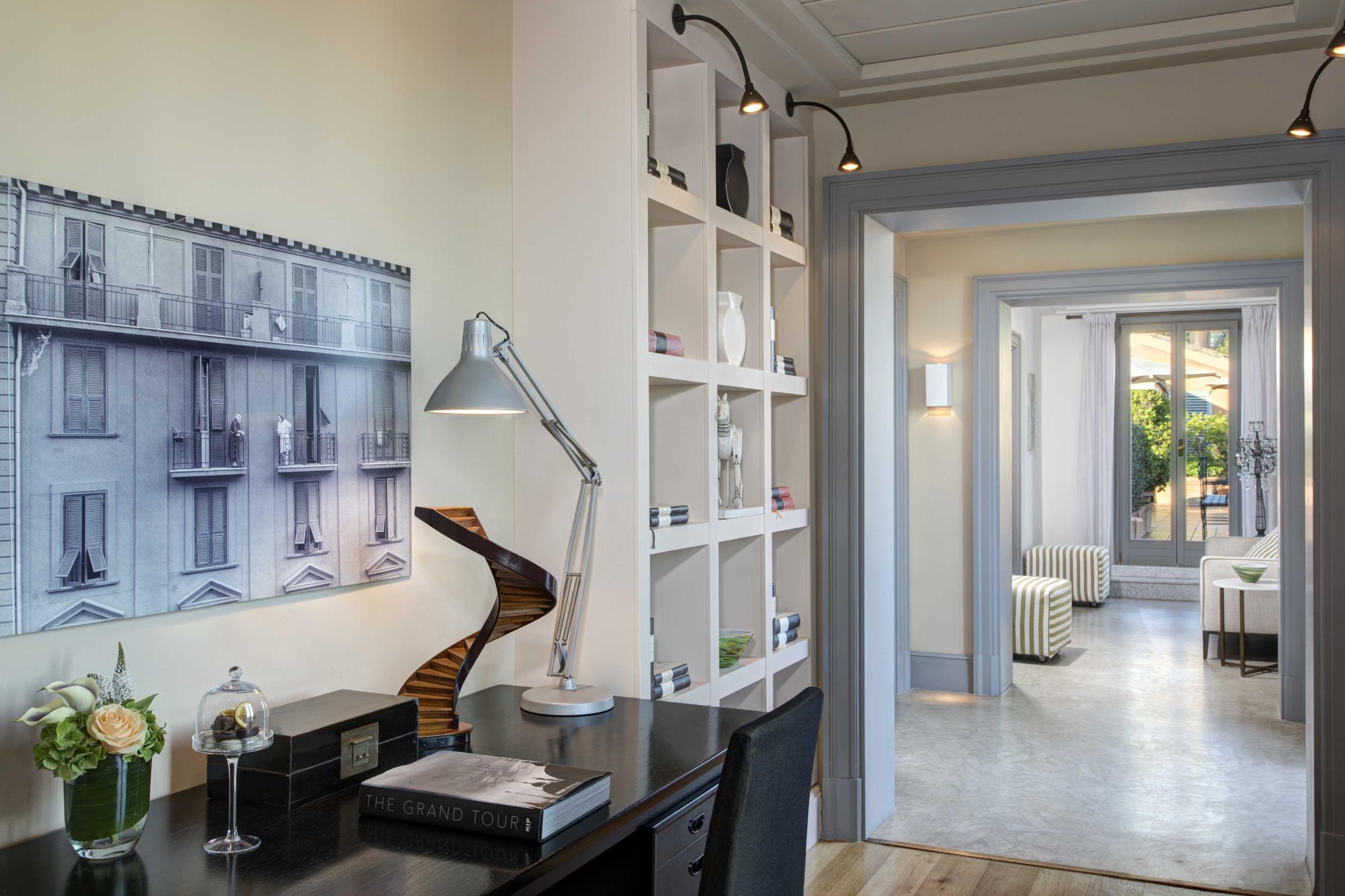 Writing desk with framed artwork, shelving, and doorway to adjoining room