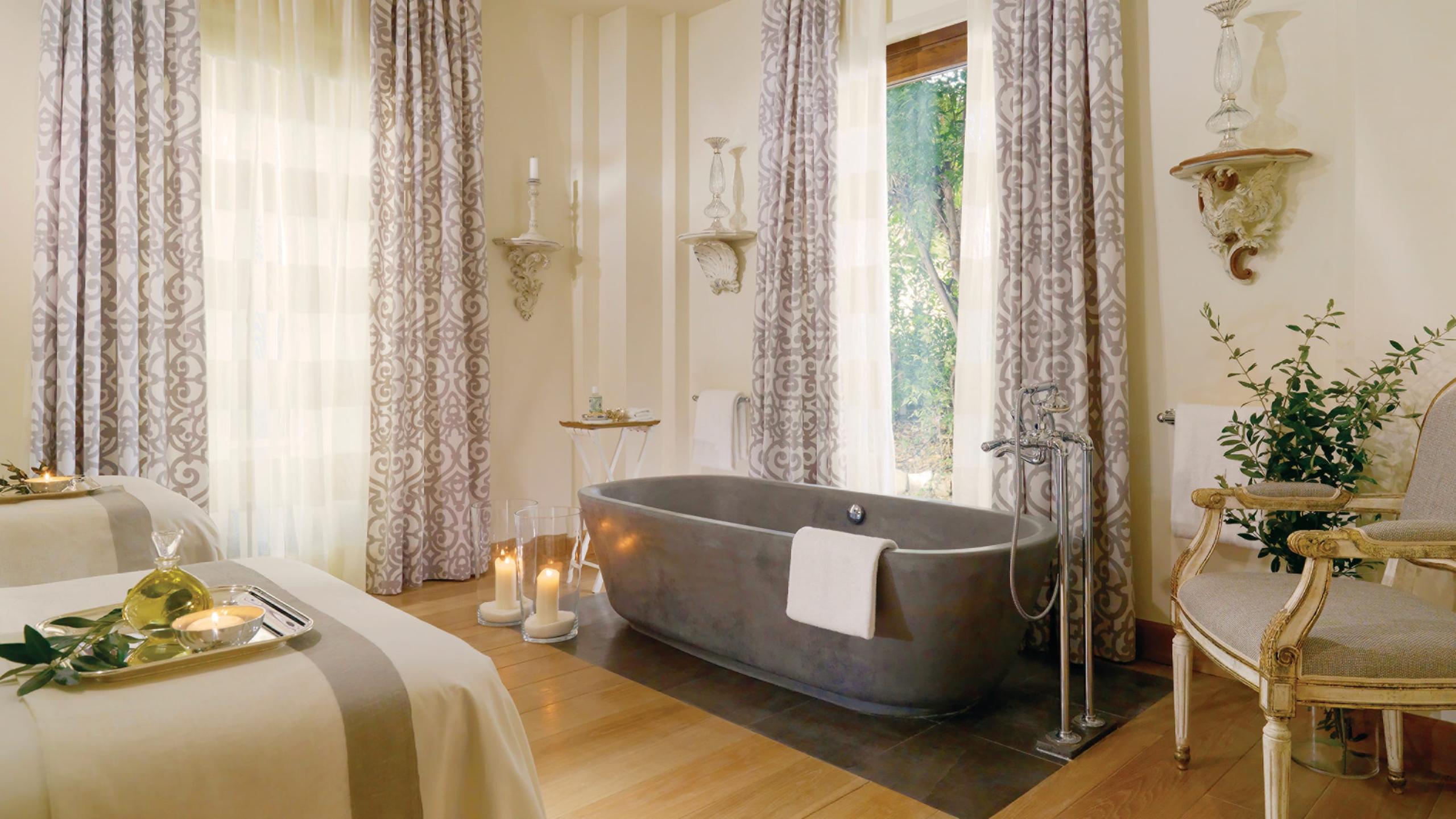 Four Seasons Hotel Firenze: spa bathroom with dark stone tub, tall windows with patterned drapery, and pale walls