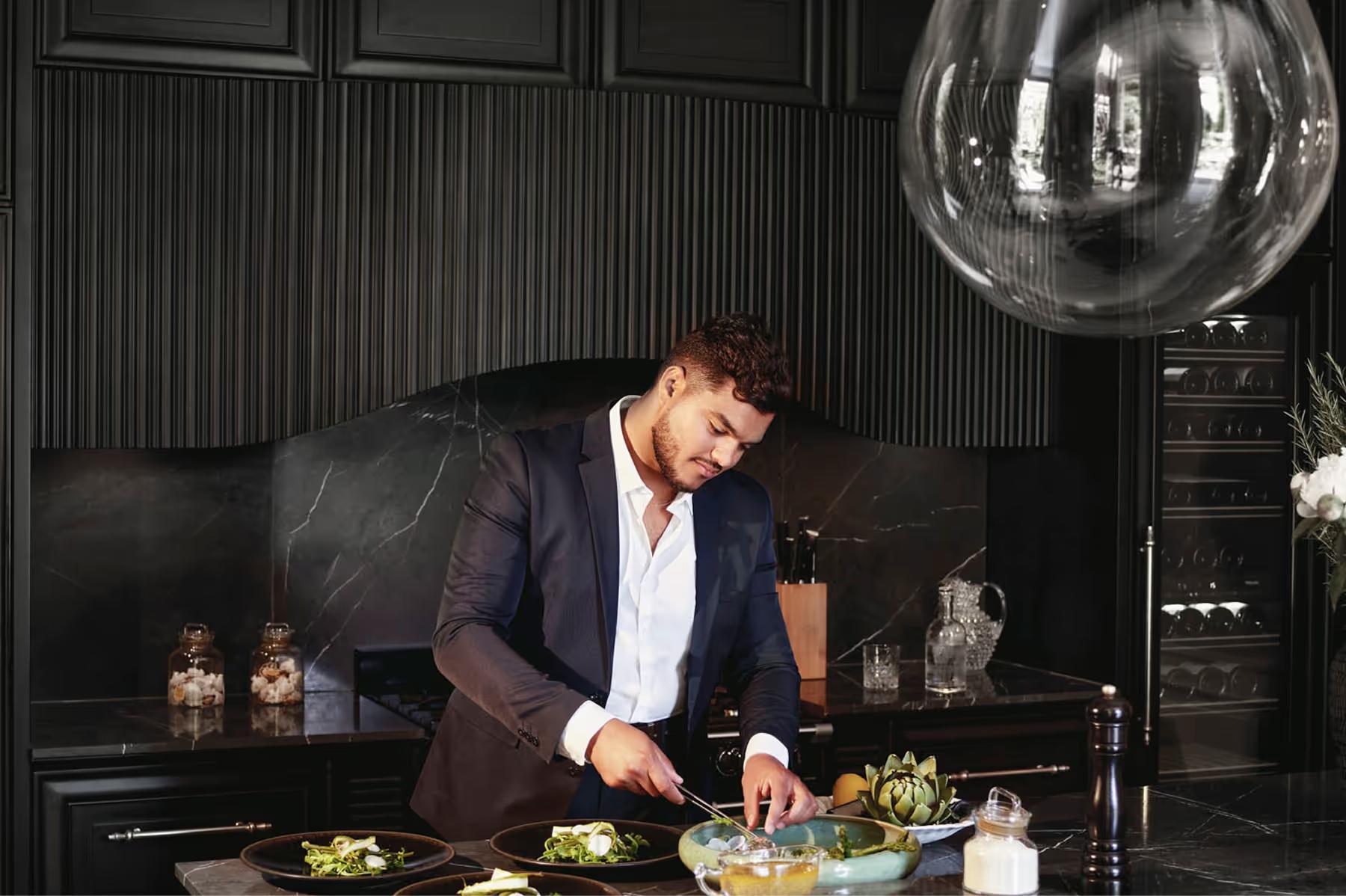 Chef in dark jacket preparing food at white countertop under pendant lighting