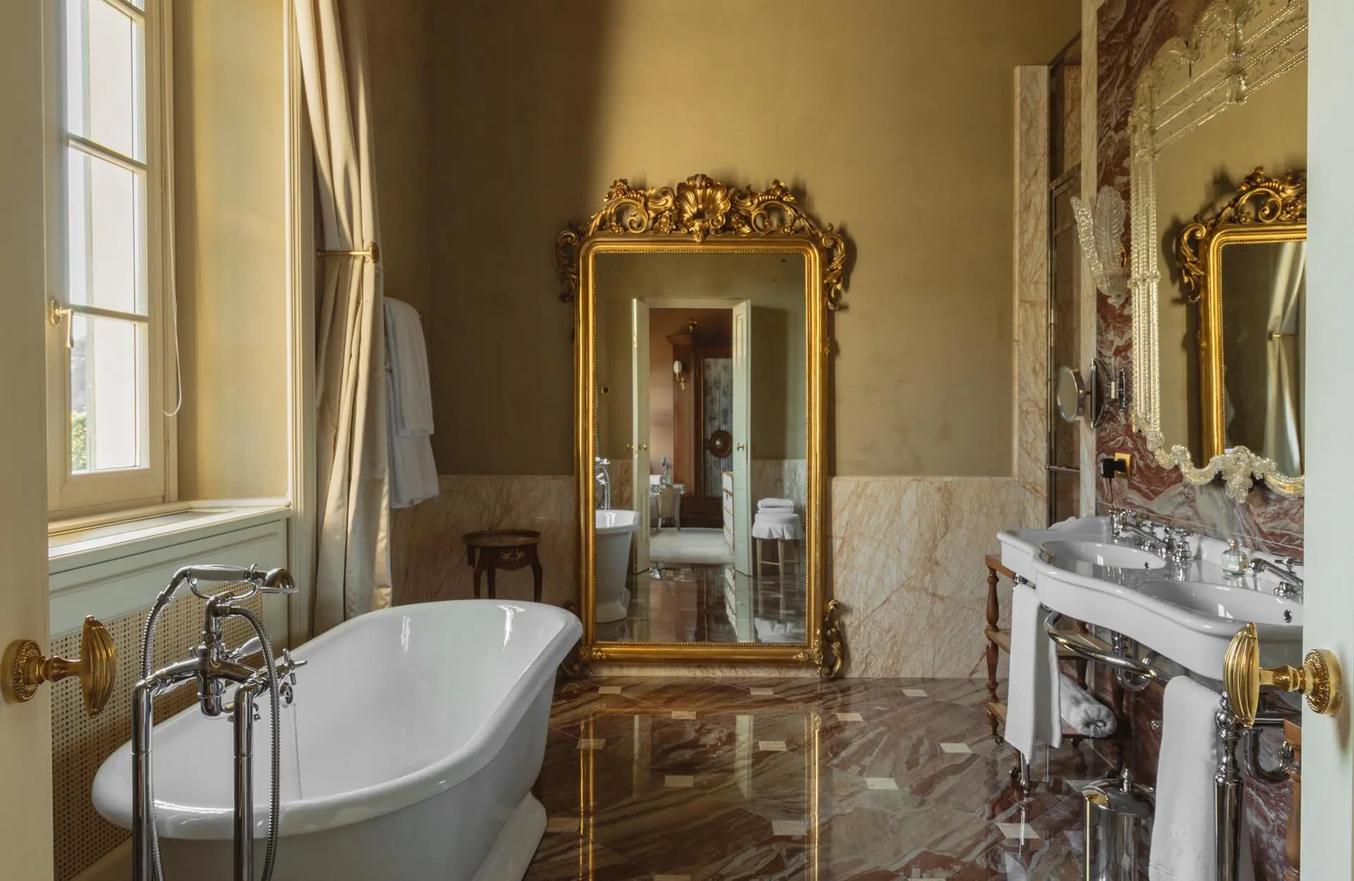 Passalacqua: a pale bathroom with freestanding tub, gold-framed mirror, and marble wainscoting