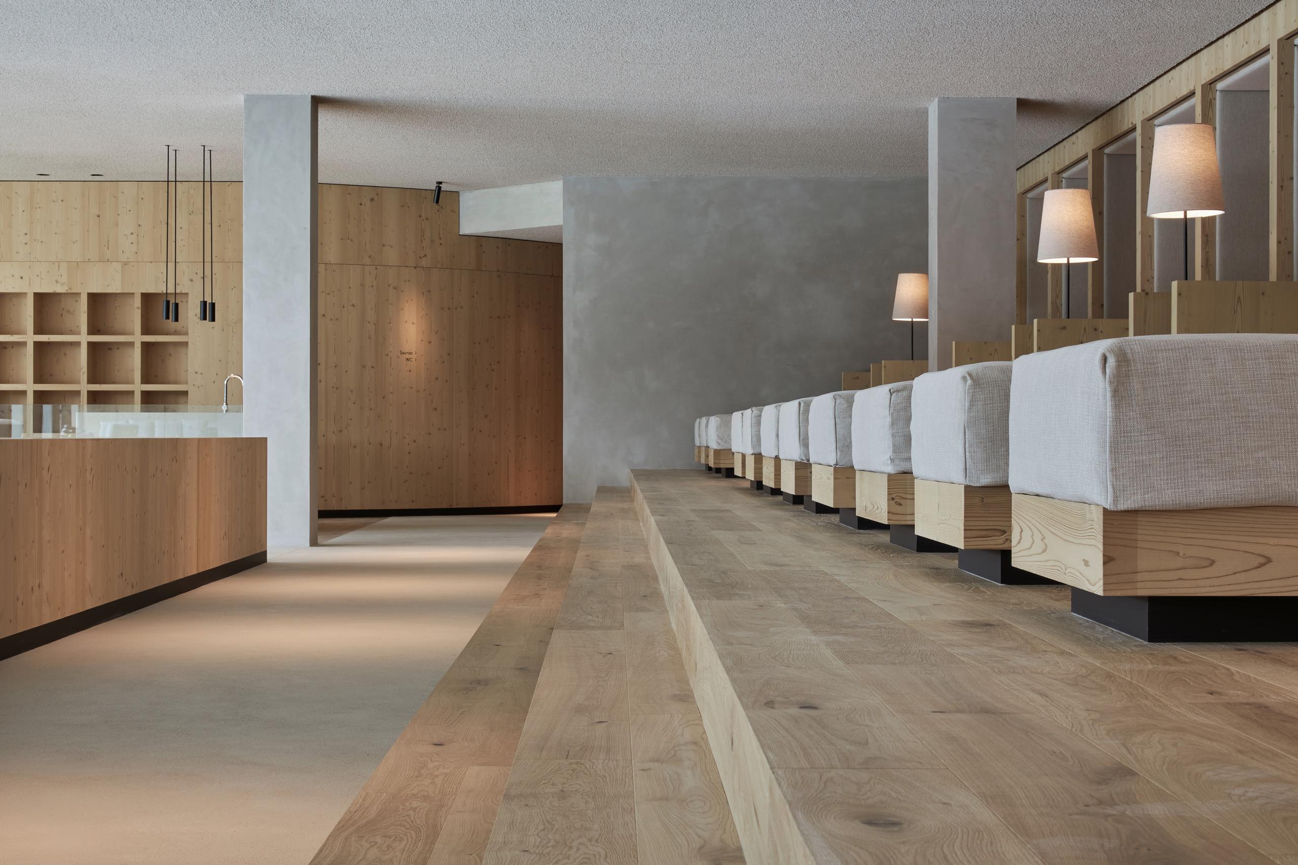 Forestis: a spa corridor with wooden and concrete finishes, lit by soft side lighting, lined with natural materials
