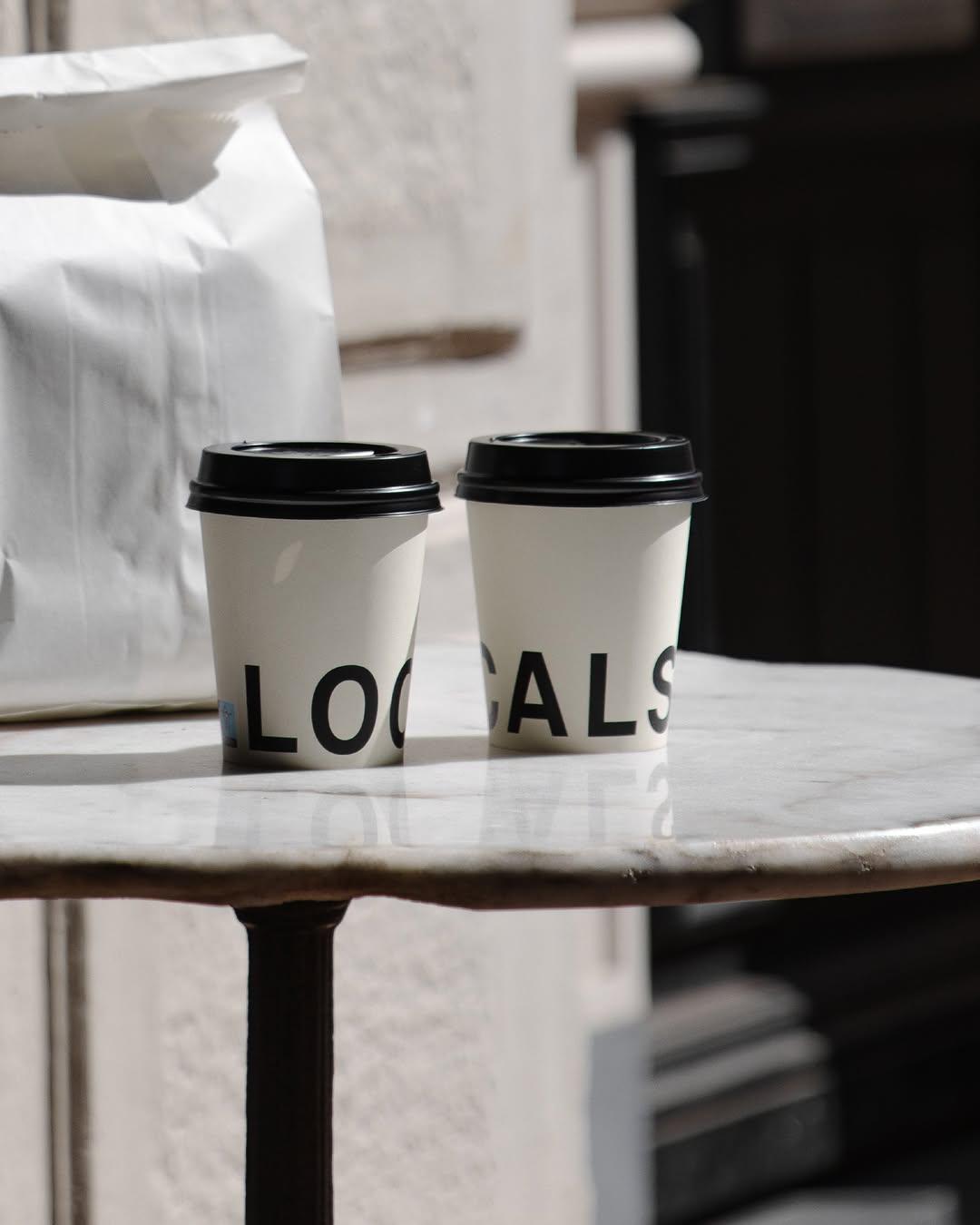 Two Locals takeaway cups on a marble table