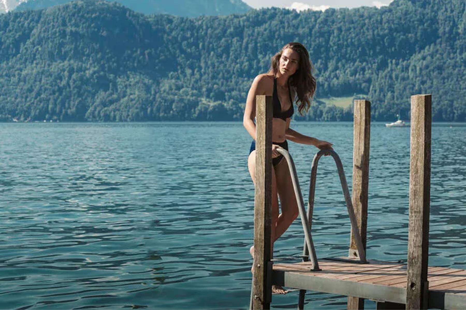 Chenot Palace Weggis: woman at lake dock in tan swimwear, Lake Lucerne, Alpine mountains behind on clear day